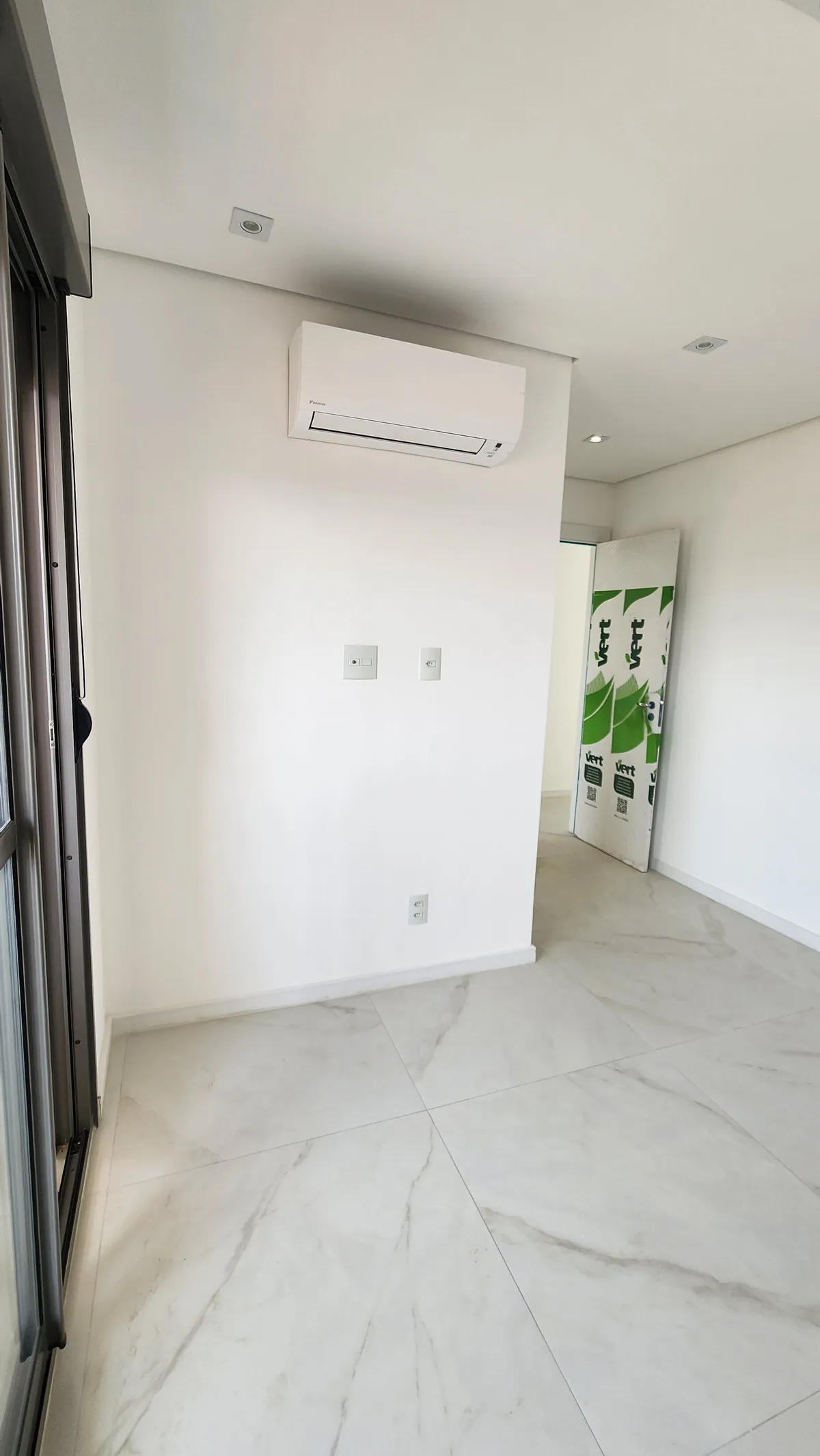 Cômodo vazio com ar-condicionado na parede branca e piso de porcelanato marmorizado, antes da reforma