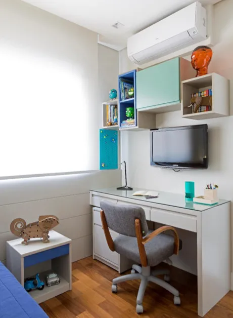 Bancada de estudo com nichos azul e verde, TV, cadeira cinza e ar-condicionado, antes da reforma