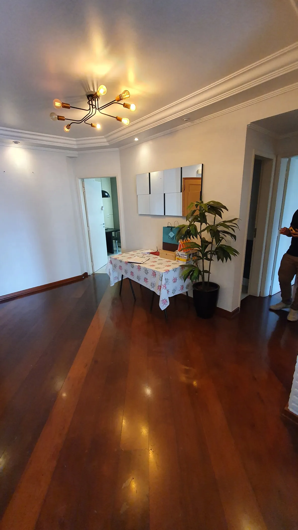 Sala vazia com piso de madeira escura, lustre de filamento e painel de espelhos na parede, antes da reforma