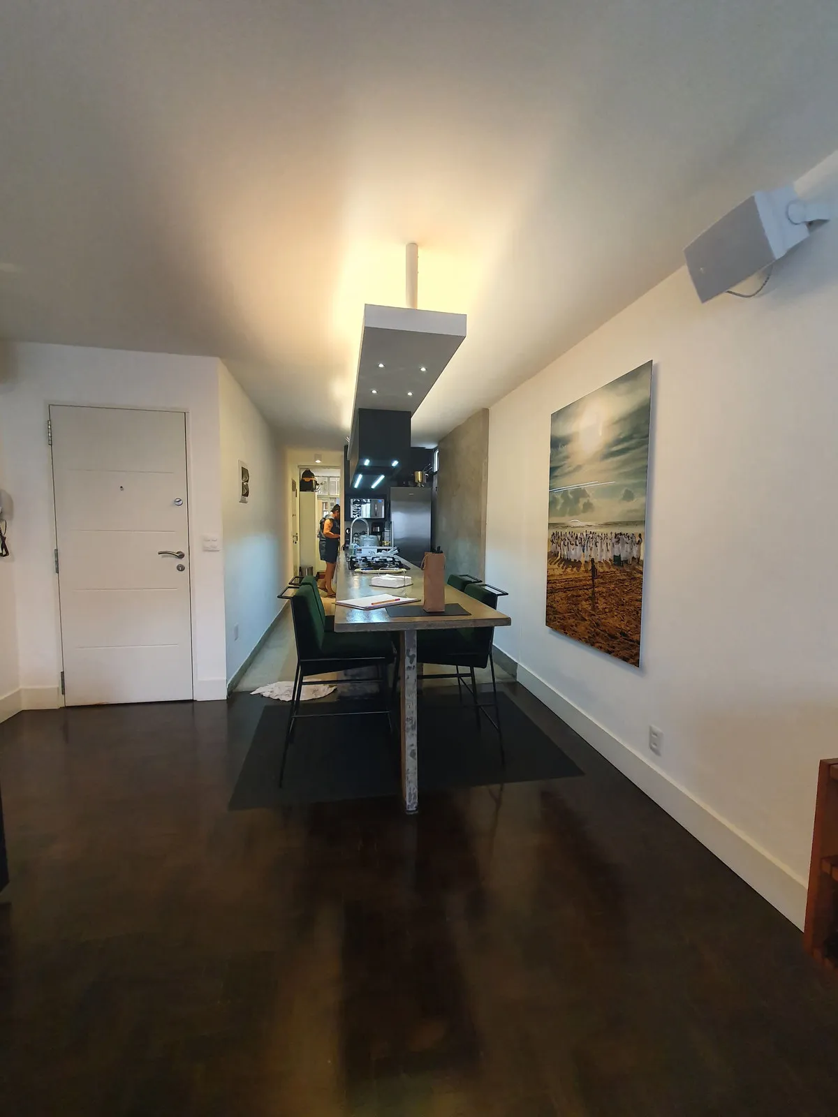 Sala de jantar com bancada de concreto e cozinha ao fundo, piso de madeira escura, antes da reforma