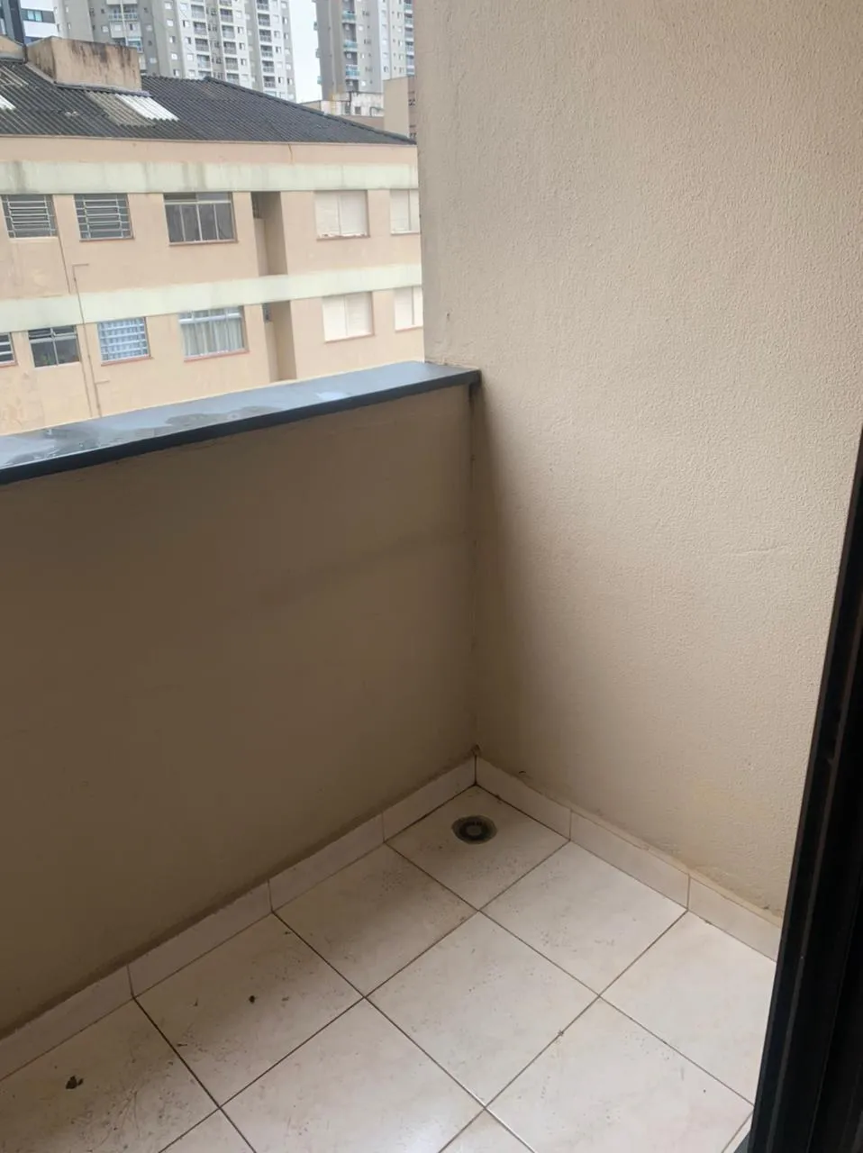 Varanda pequena com paredes de textura bege, piso de cerâmica e vista de prédios, antes da reforma