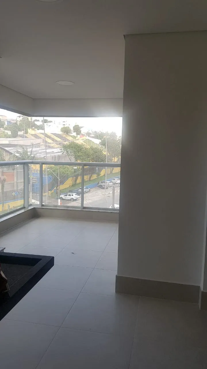 Varanda com bancada de granito, guarda-corpo de vidro e ampla vista da cidade, piso claro, antes da reforma