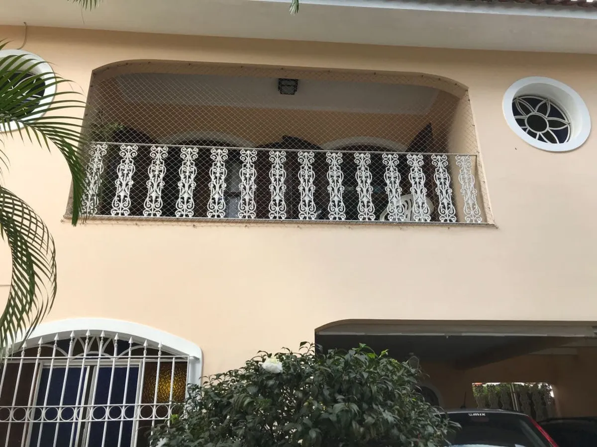 Fachada bege com sacada de guarda-corpo de ferro branco, janela redonda e garagem, antes da reforma