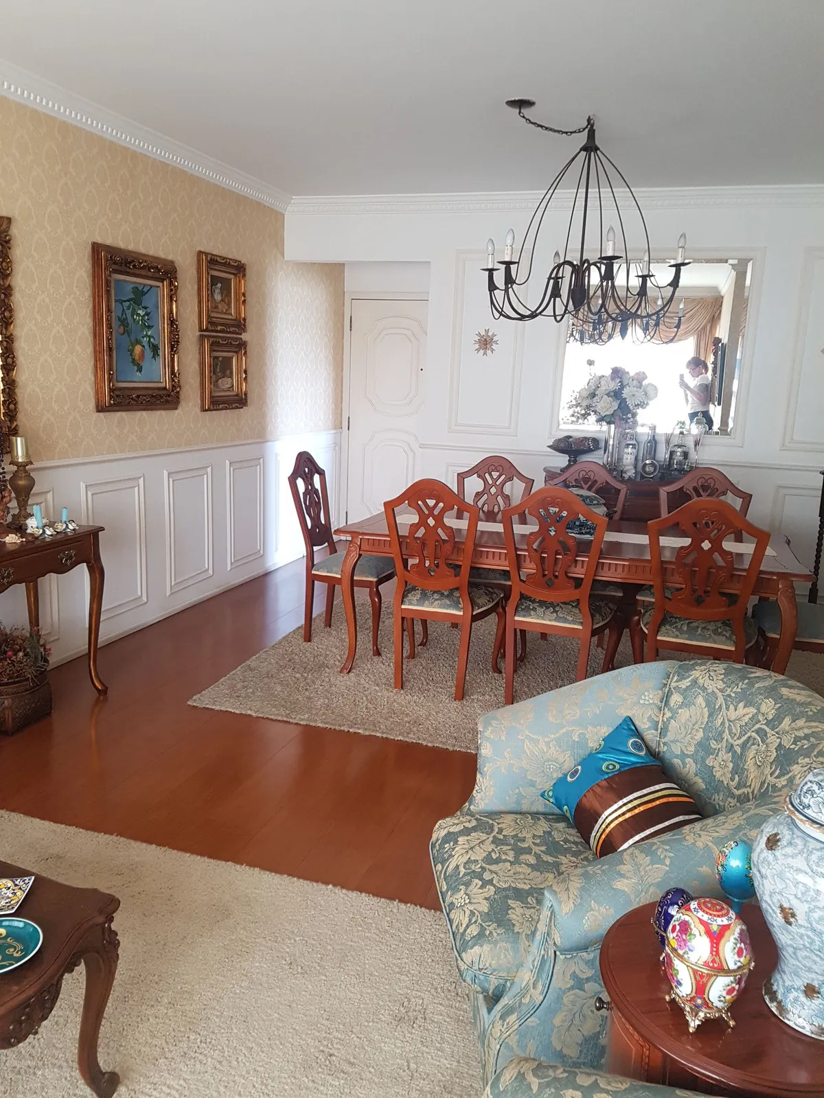 Sala de jantar e estar integradas, com papel de parede bege, poltronas floral azul e piso de madeira envernizado, antes da reforma