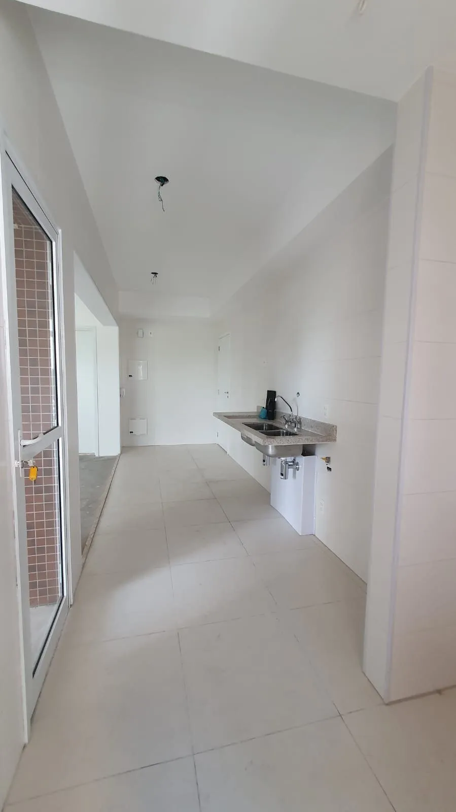 Cozinha em corredor com bancada de granito, cuba provisória, azulejo branco e piso claro, antes da reforma