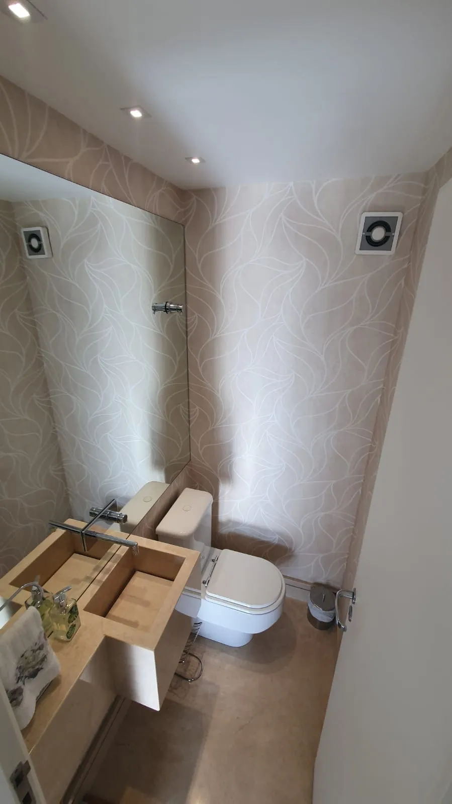 Lavabo antigo com papel de parede de folhas bege, espelho grande e bancada de mármore, antes da reforma