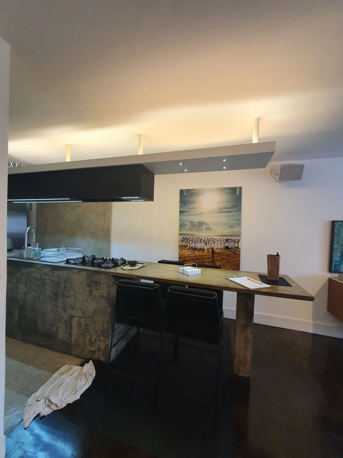 Cozinha antiga com bancada e revestimento de concreto aparente, coifa preta e cooktop, antes da reforma