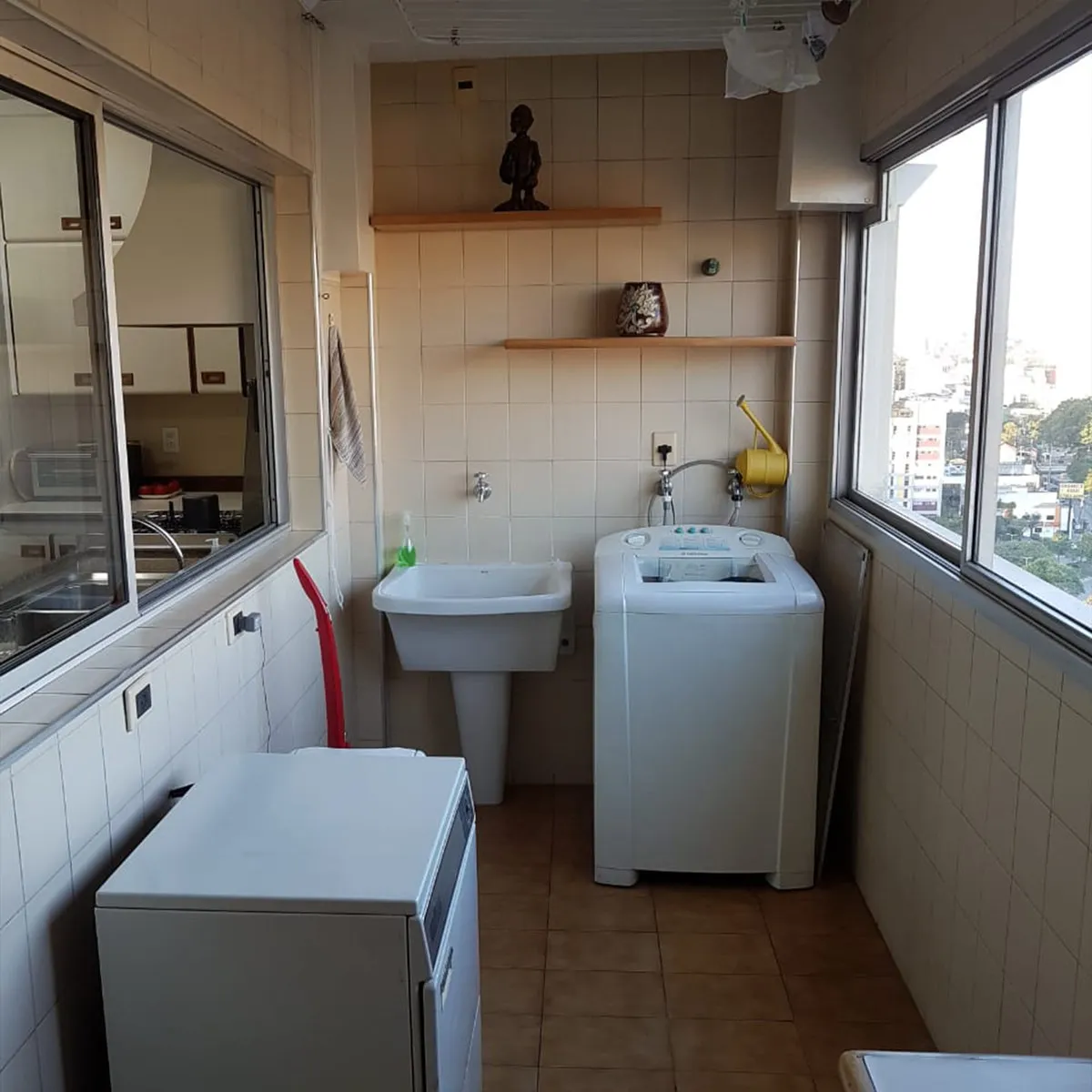 Área de serviço antiga com azulejo branco, tanque de louça e máquina de lavar, antes da reforma