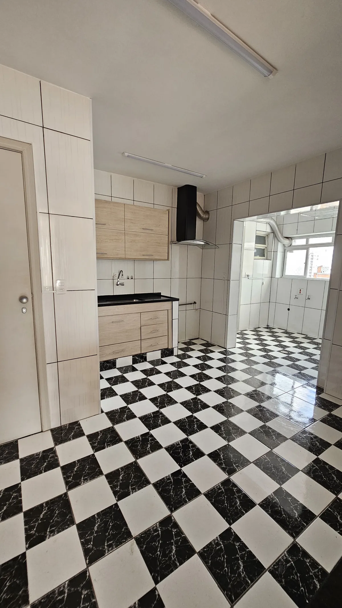 Cozinha antiga com piso xadrez preto e branco, azulejo branco, armários de madeira clara e coifa preta, antes da reforma