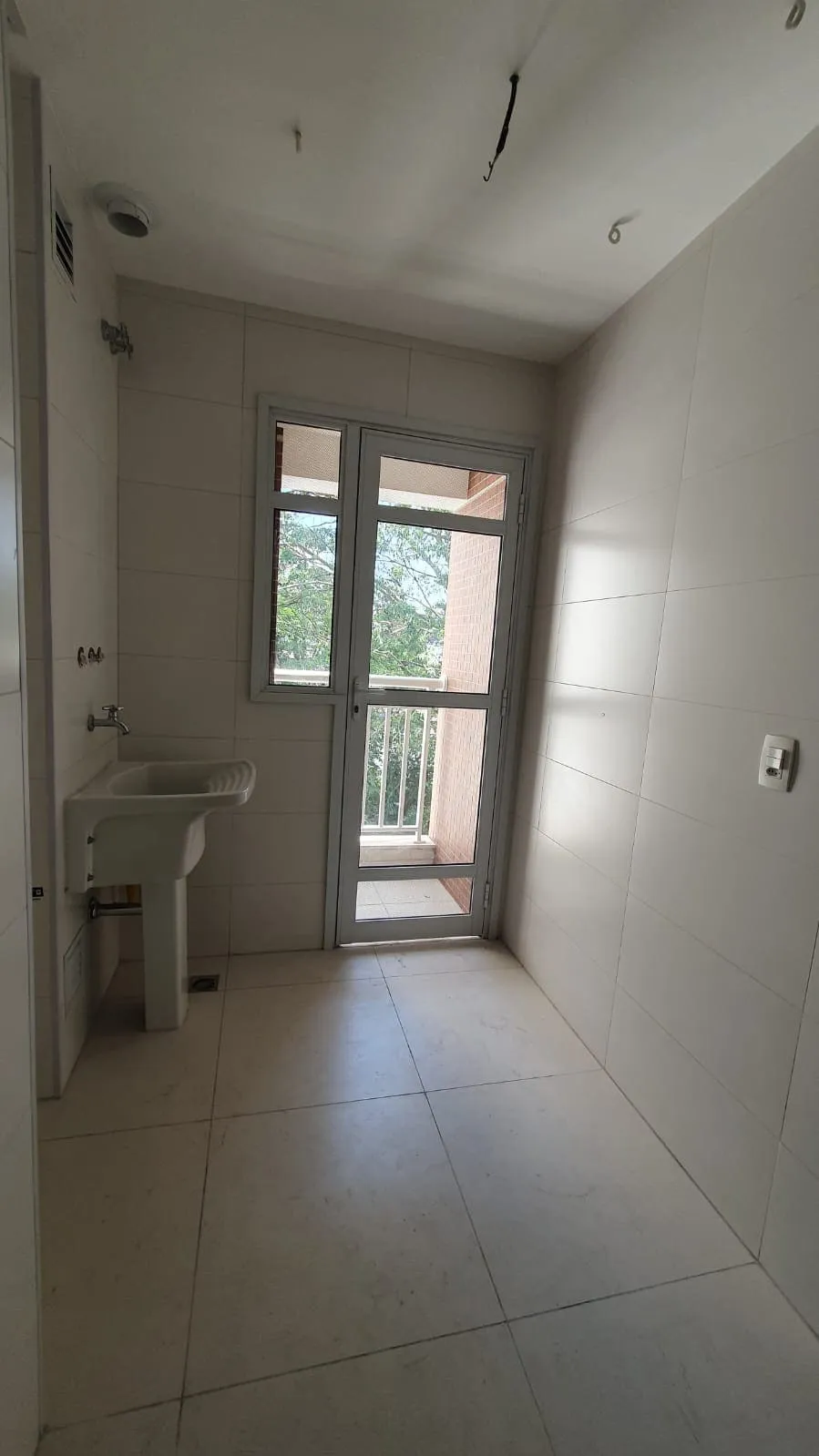 Área de serviço com tanque de louça, revestimento branco e porta de vidro pra varanda, antes da reforma