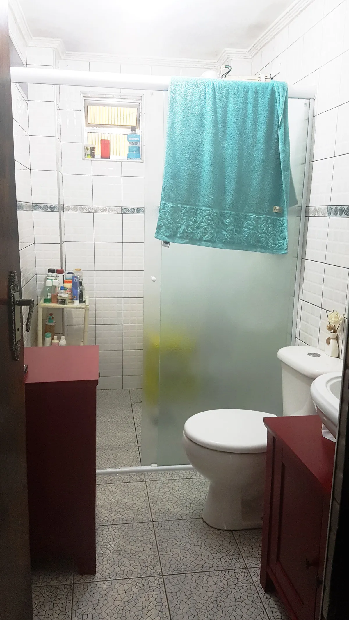 Banheiro antigo com azulejo branco, box de vidro, gabinetes vermelhos e piso de caco de mármore, antes da reforma