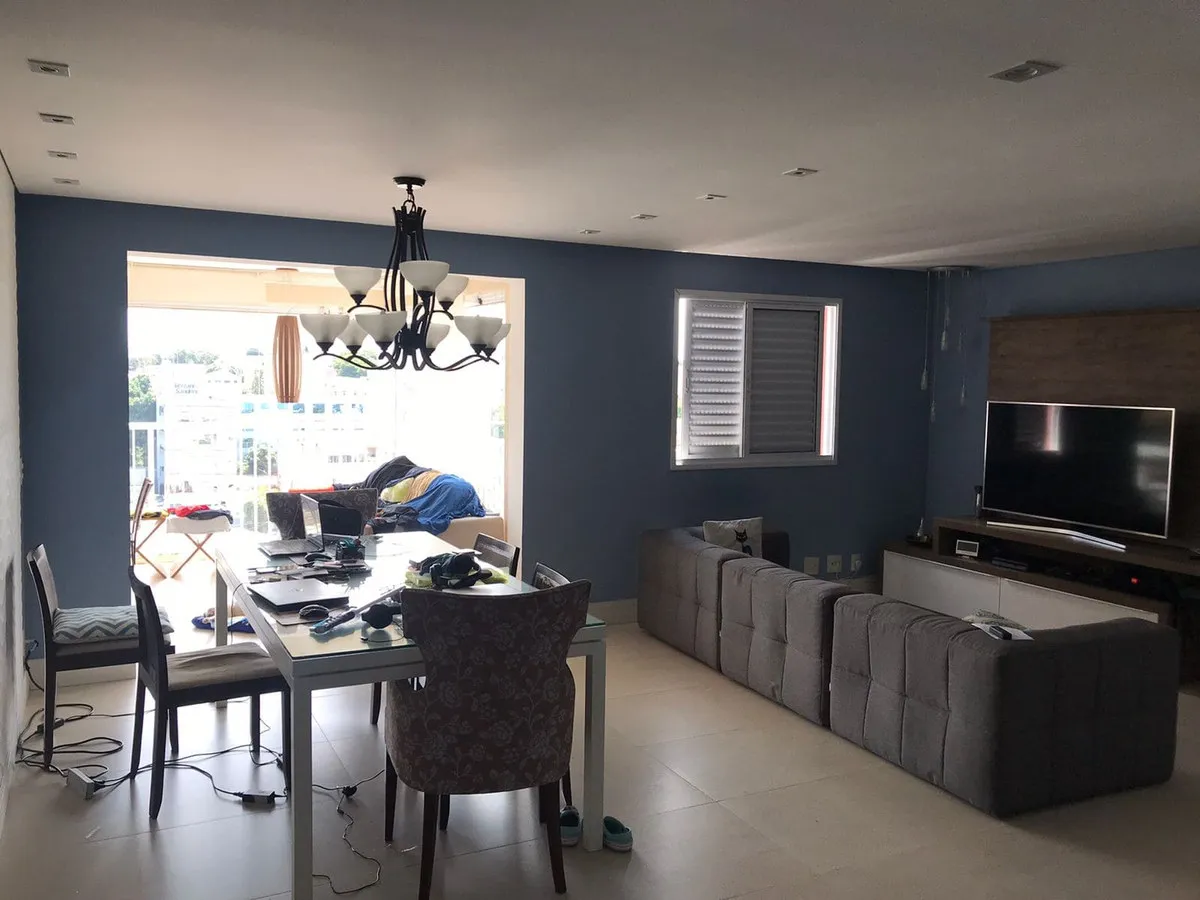 Sala integrada com paredes azuis, mesa de jantar junto à varanda, sofá cinza e TV, antes da reforma