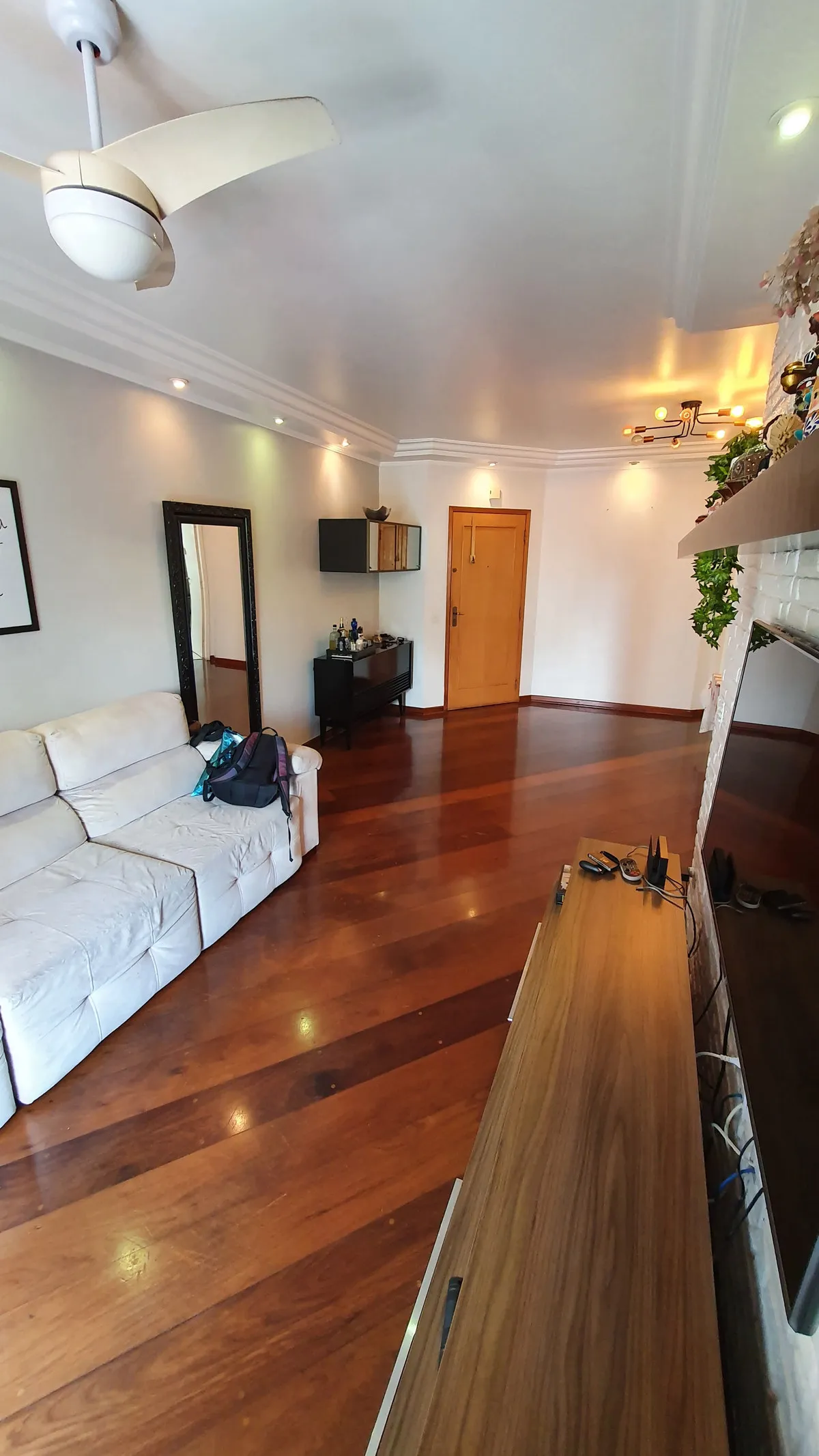 Sala de estar com sofá branco, espelho de chão, aparador preto e porta de madeira, antes da reforma