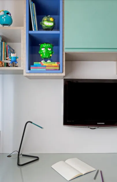 Detalhe de nicho azul com livros e bonecos, armário verde-água, TV Samsung e luminária sobre a bancada, antes da reforma