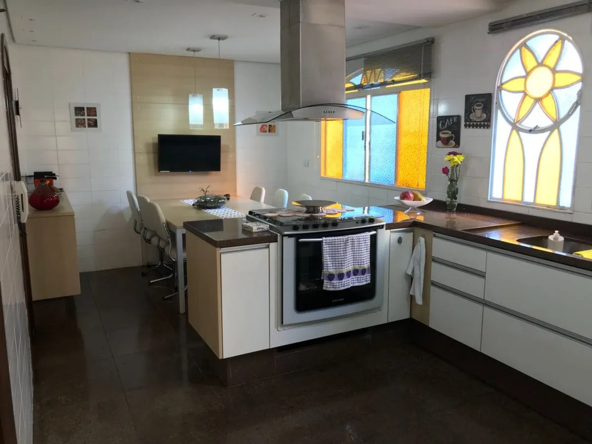 Cozinha antiga com armários brancos, fogão na ilha, coifa inox e piso escuro, antes da reforma