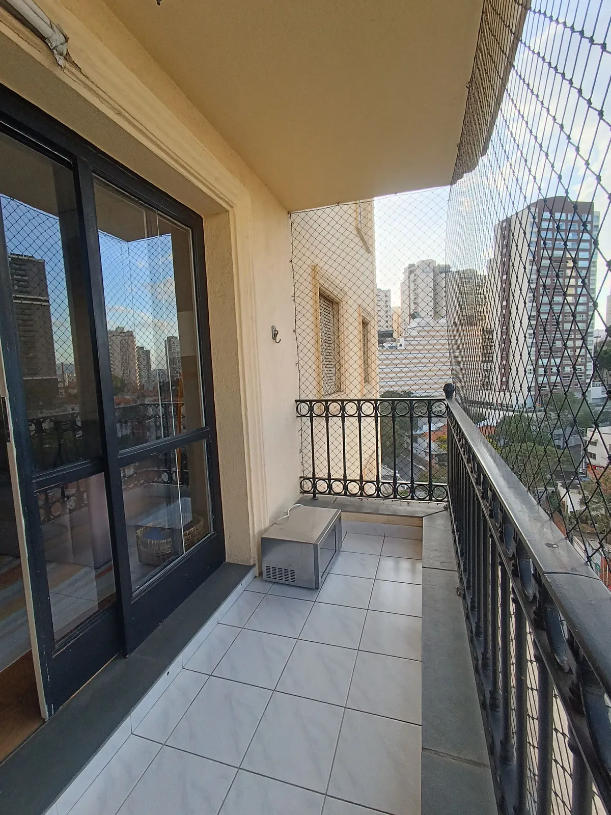 Varanda estreita com piso cinza, guarda-corpo de ferro, tela de proteção e vista da cidade, antes da reforma
