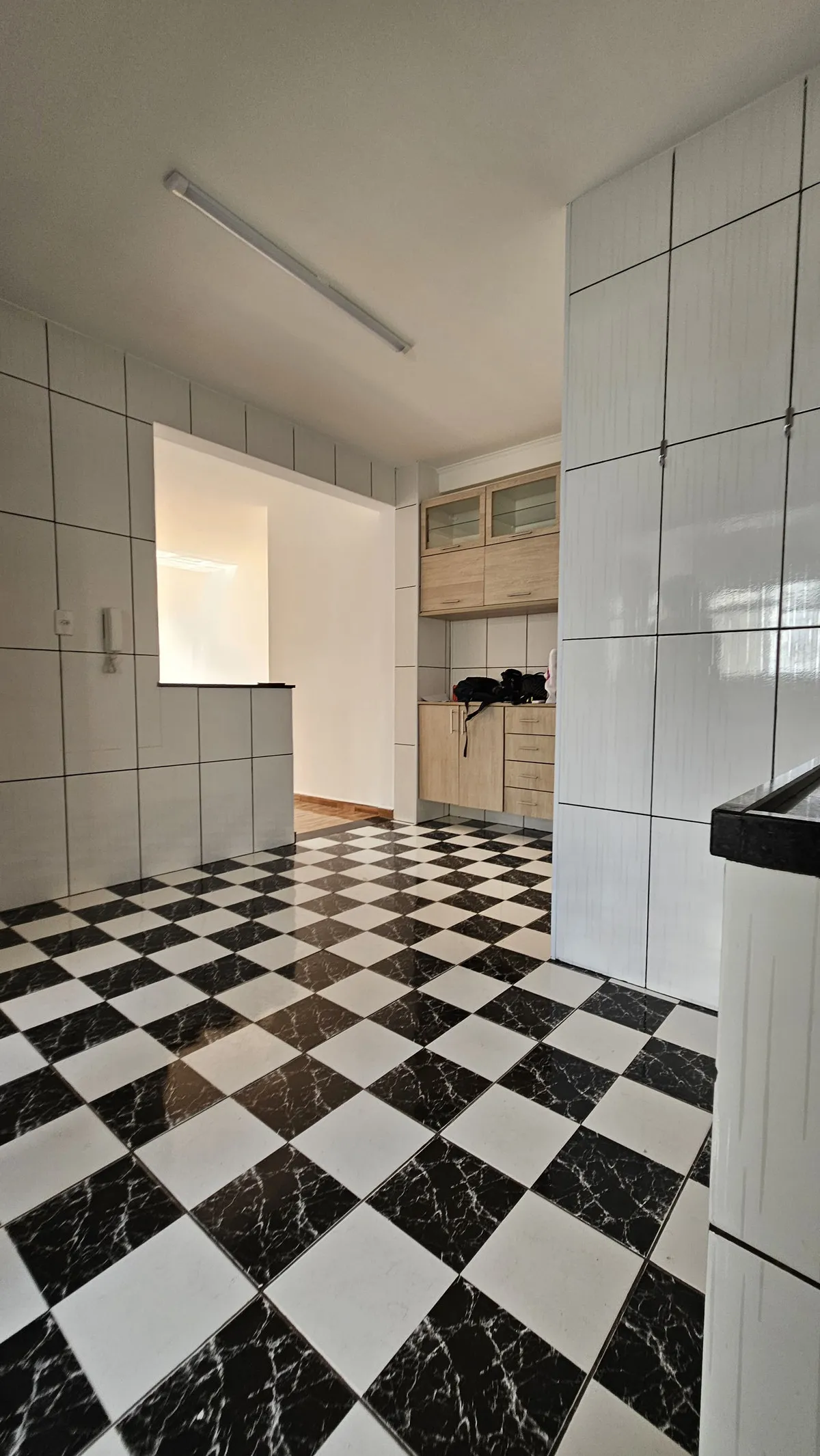 Cozinha com piso xadrez preto e branco, paredes de azulejo branco e marcenaria de madeira clara, antes da reforma