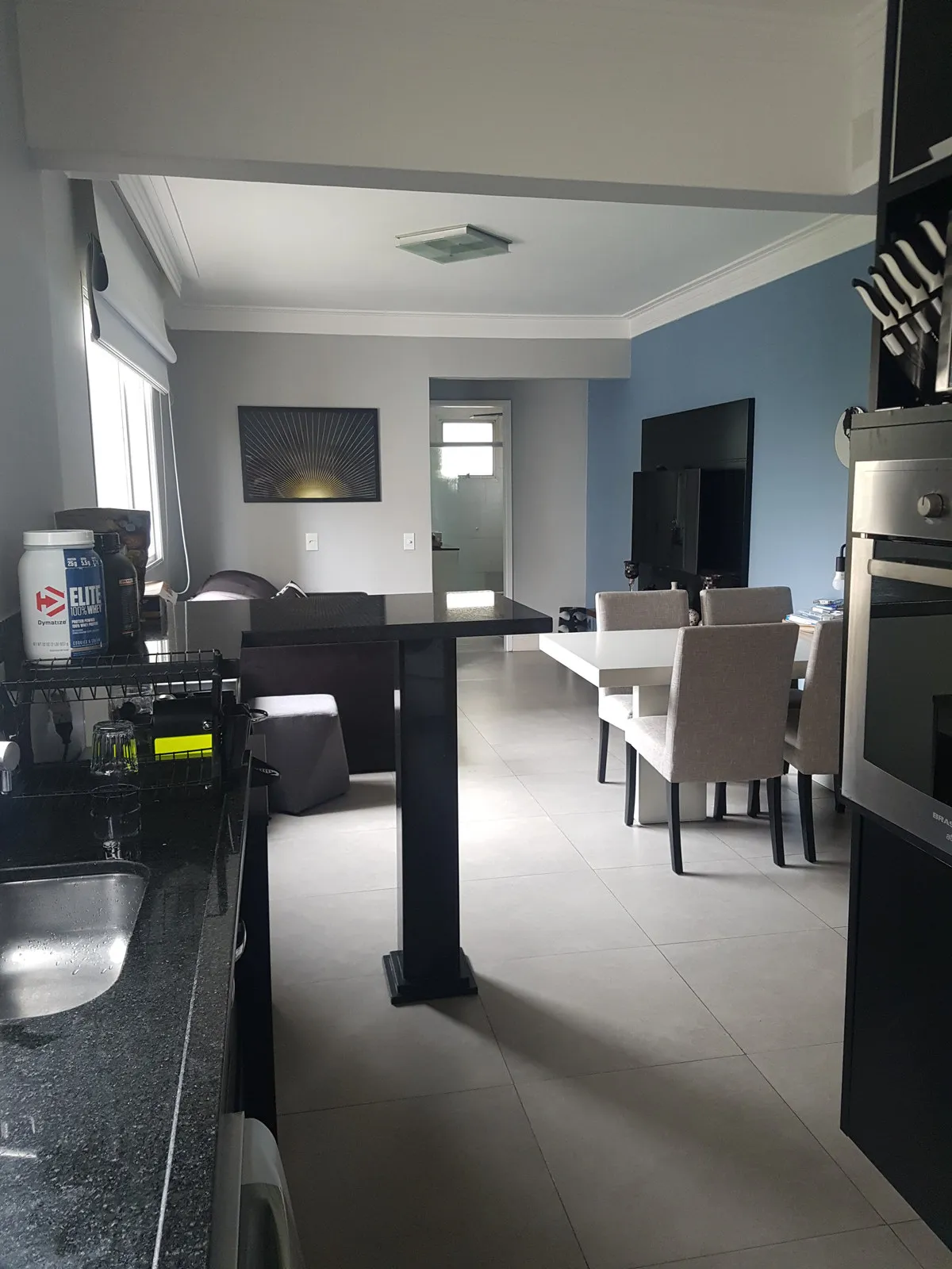 Vista da cozinha para sala e jantar integrados com parede azul, mesa bistrô preta e cadeiras cinza, antes da reforma