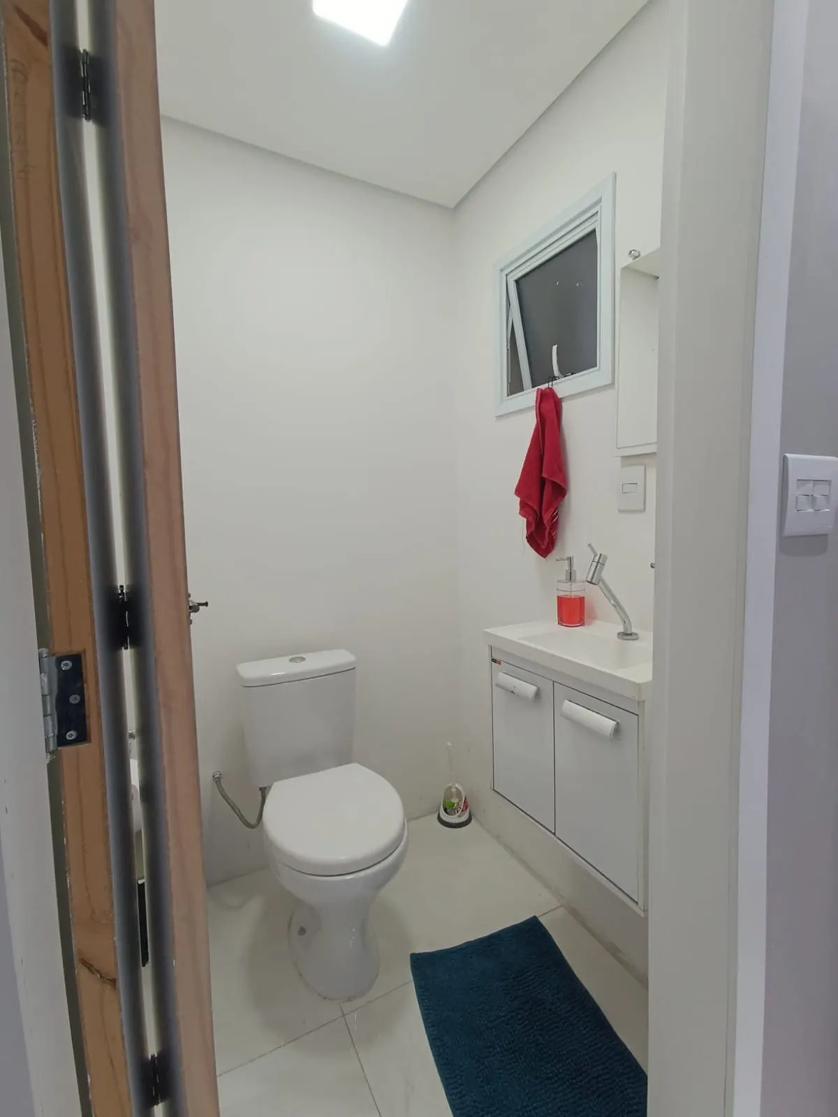 Lavabo branco com vaso, gabinete suspenso e janela basculante, antes da reforma