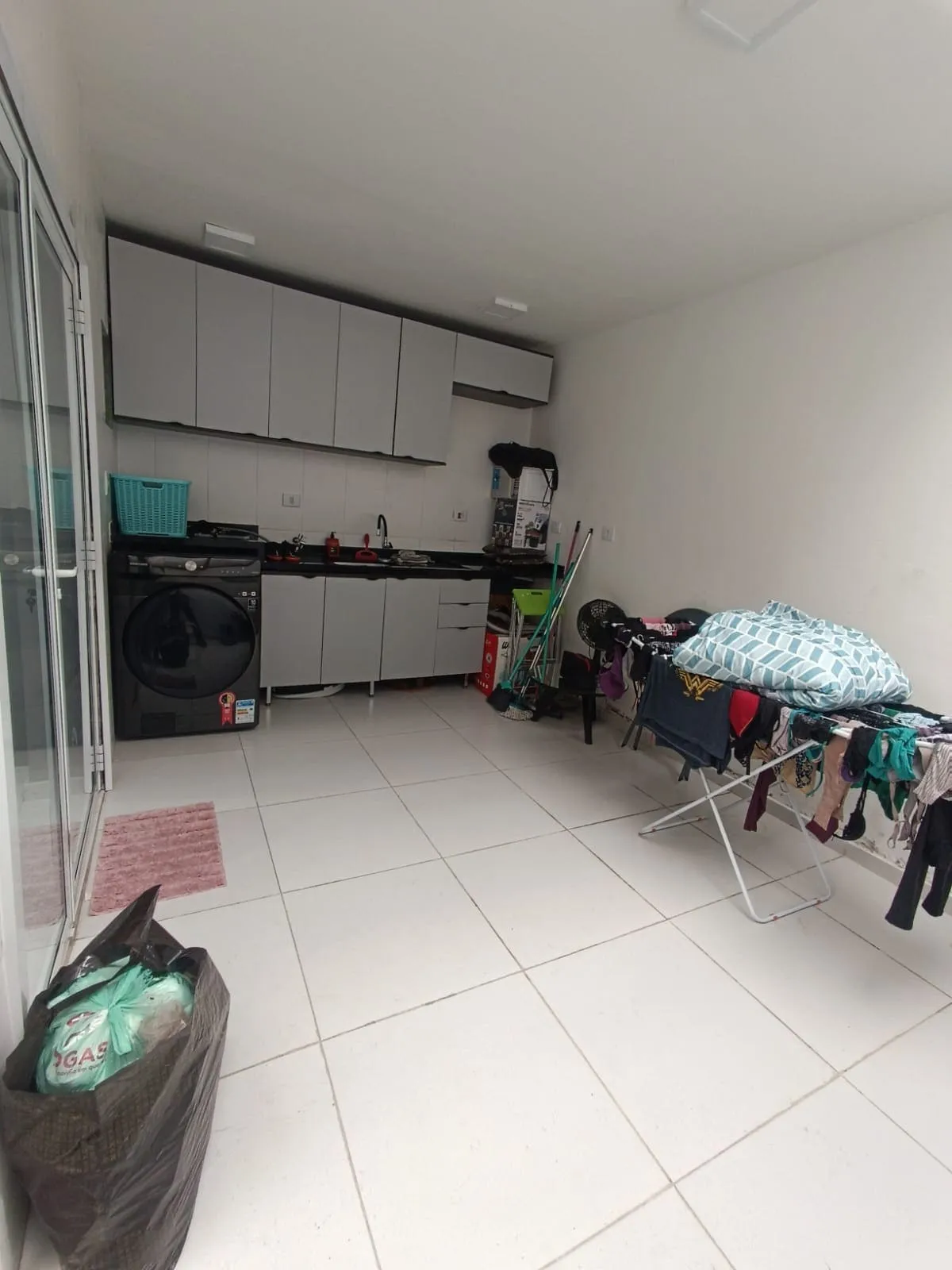 Área de serviço com armários cinza, lavadora e varal cheio de roupas, antes da reforma