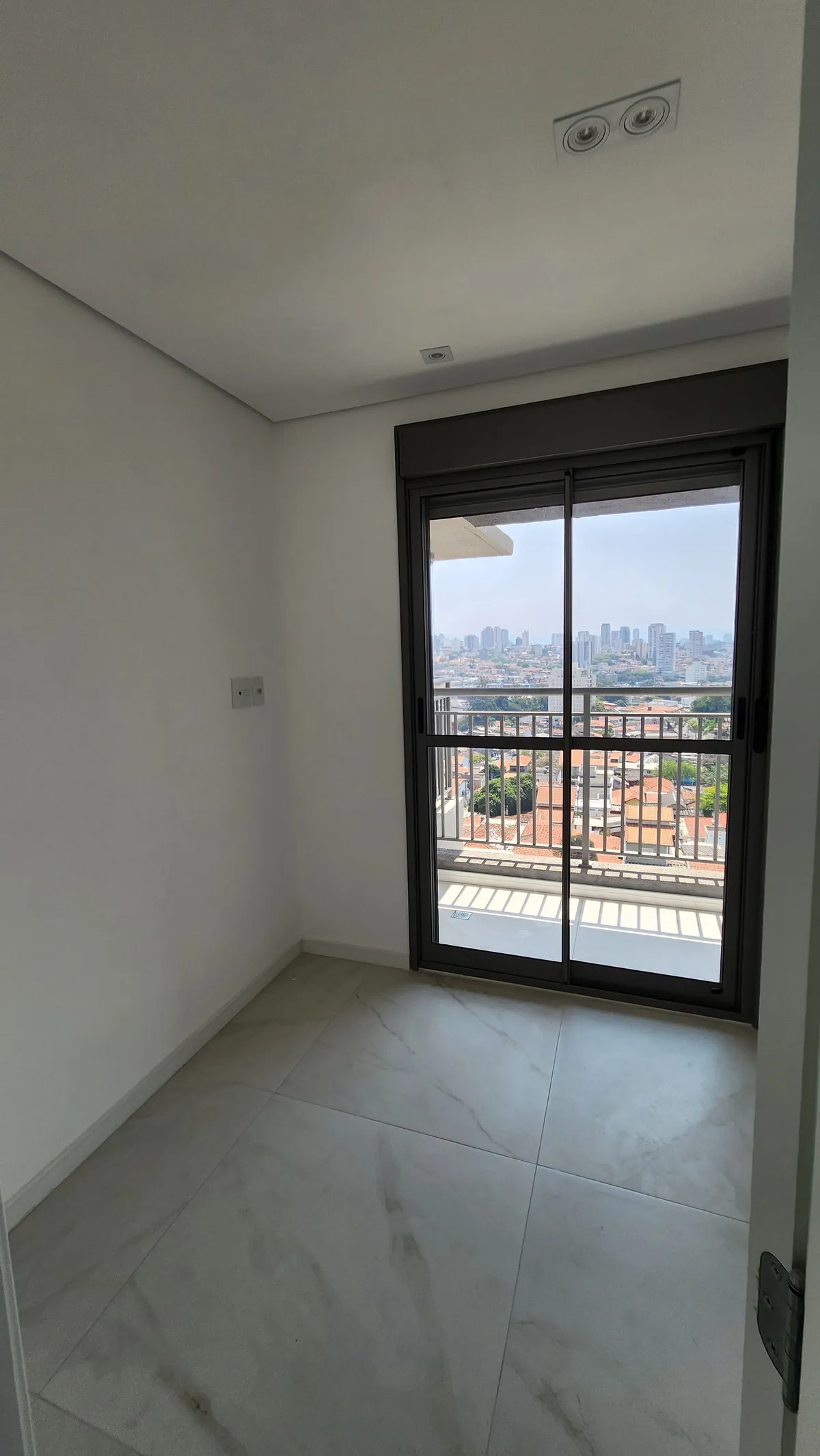 Quarto vazio com porta de vidro para a sacada e vista da cidade, antes da reforma