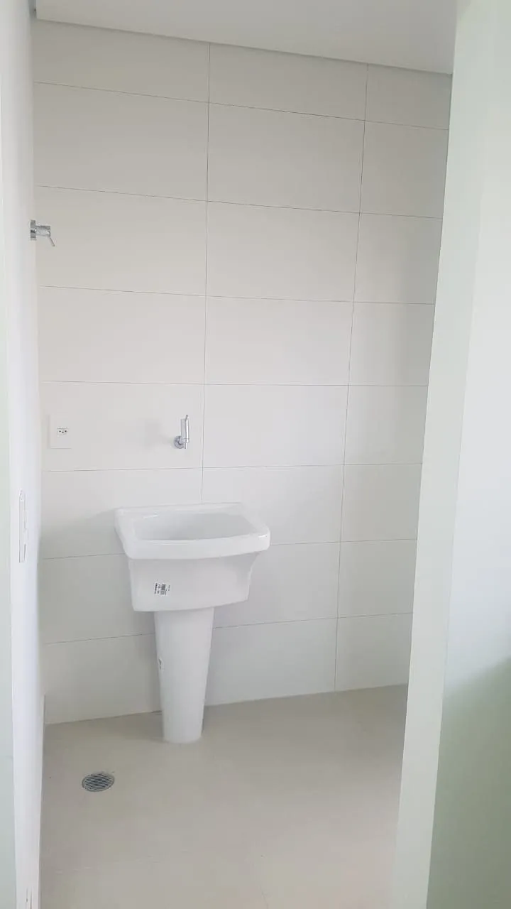Área de serviço com paredes de azulejo branco e tanque de louça fixado na parede, antes da reforma