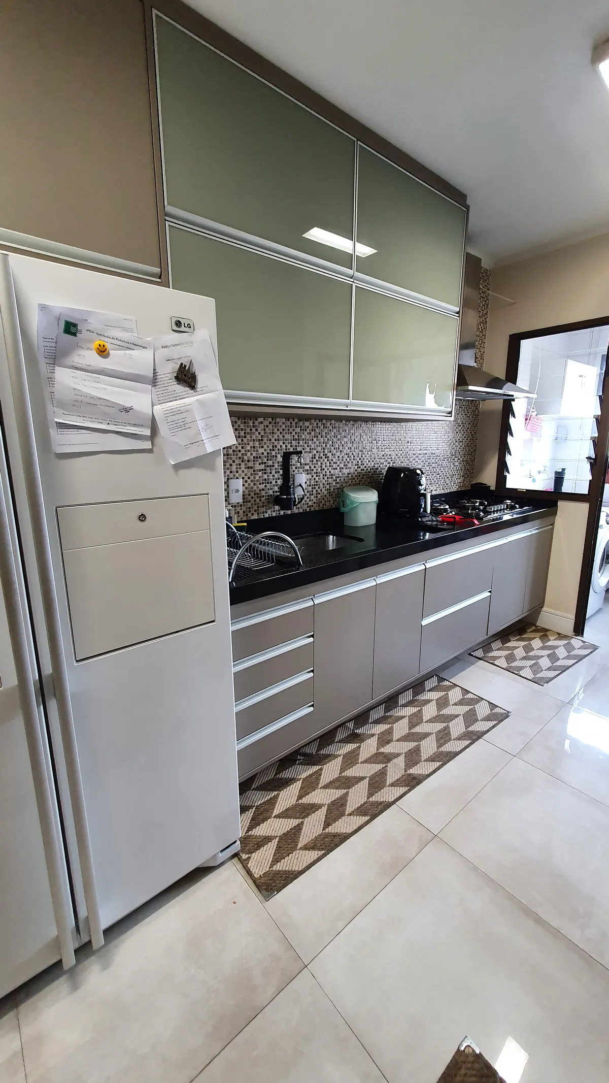 Cozinha com armários de vidro verde, bancada de granito preto e pastilha na parede, antes da reforma
