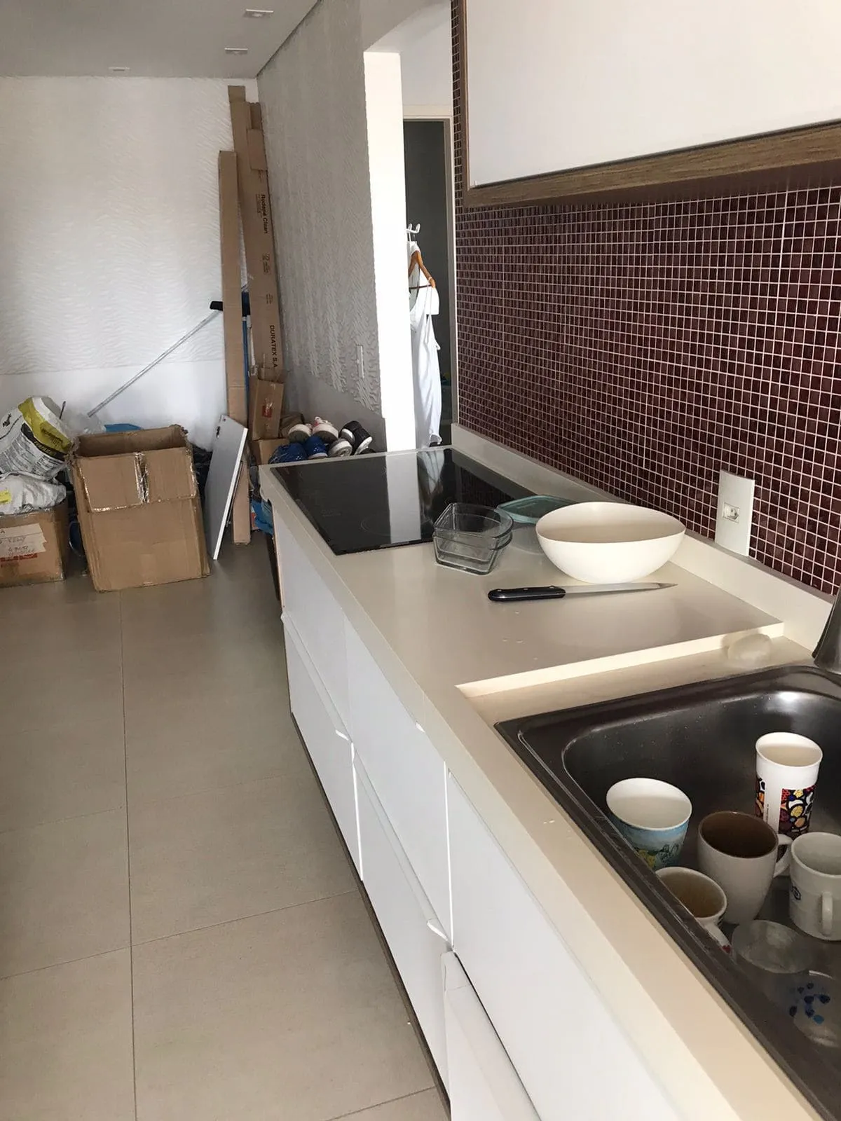 Cozinha estreita com pastilhas vinho, armários brancos e caixas de mudança amontoadas, antes da reforma