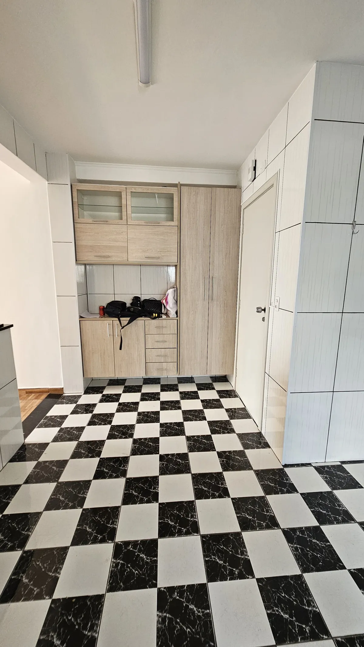 Cozinha com piso xadrez preto e branco, armários brancos altos e marcenaria de madeira clara, antes da reforma