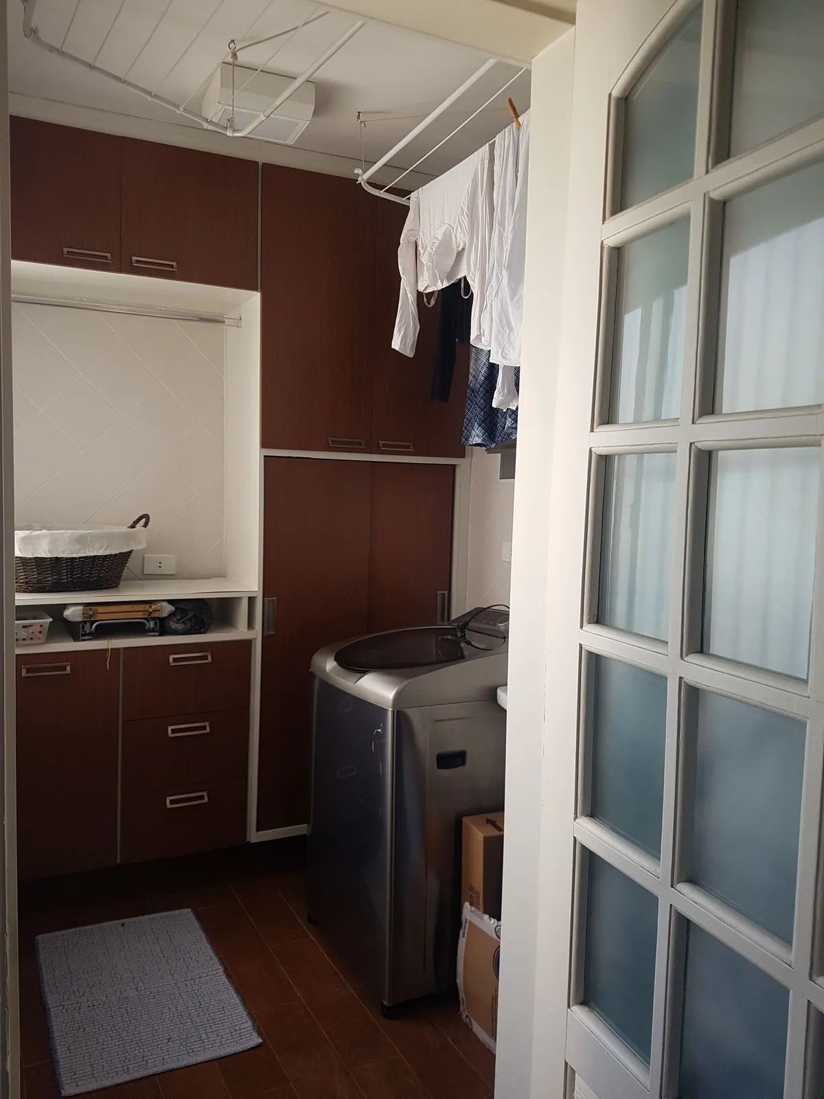 Área de serviço com armários de madeira escura, máquina de lavar e roupa no varal, antes da reforma