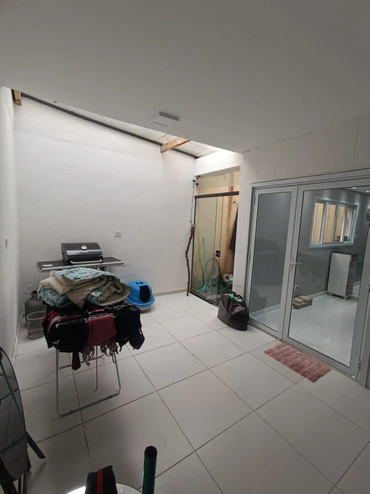 Área externa coberta com churrasqueira, varal e porta de vidro, piso branco, antes da reforma