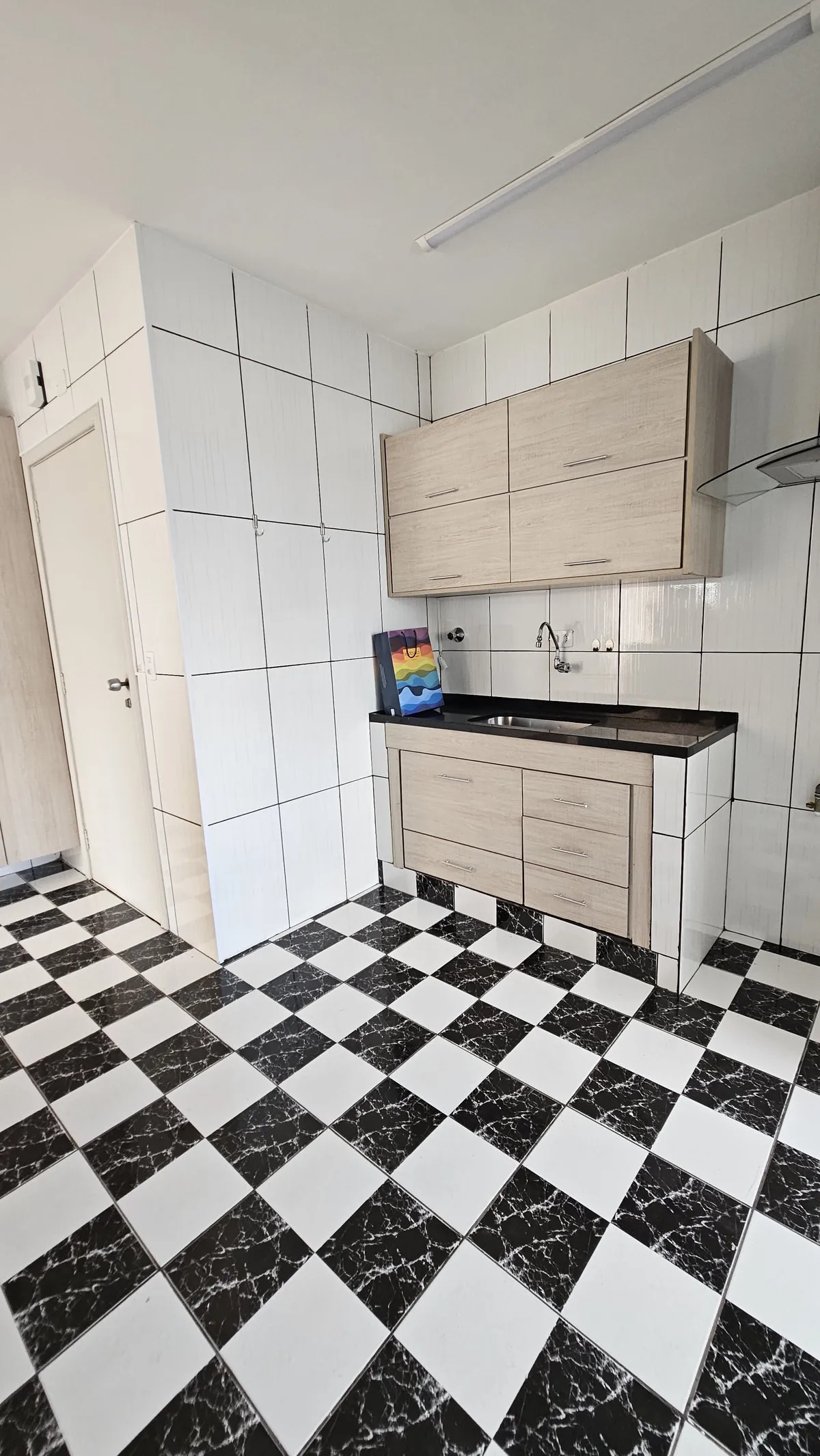 Cozinha com piso xadrez preto e branco, bancada de granito preto e armários de madeira clara, antes da reforma