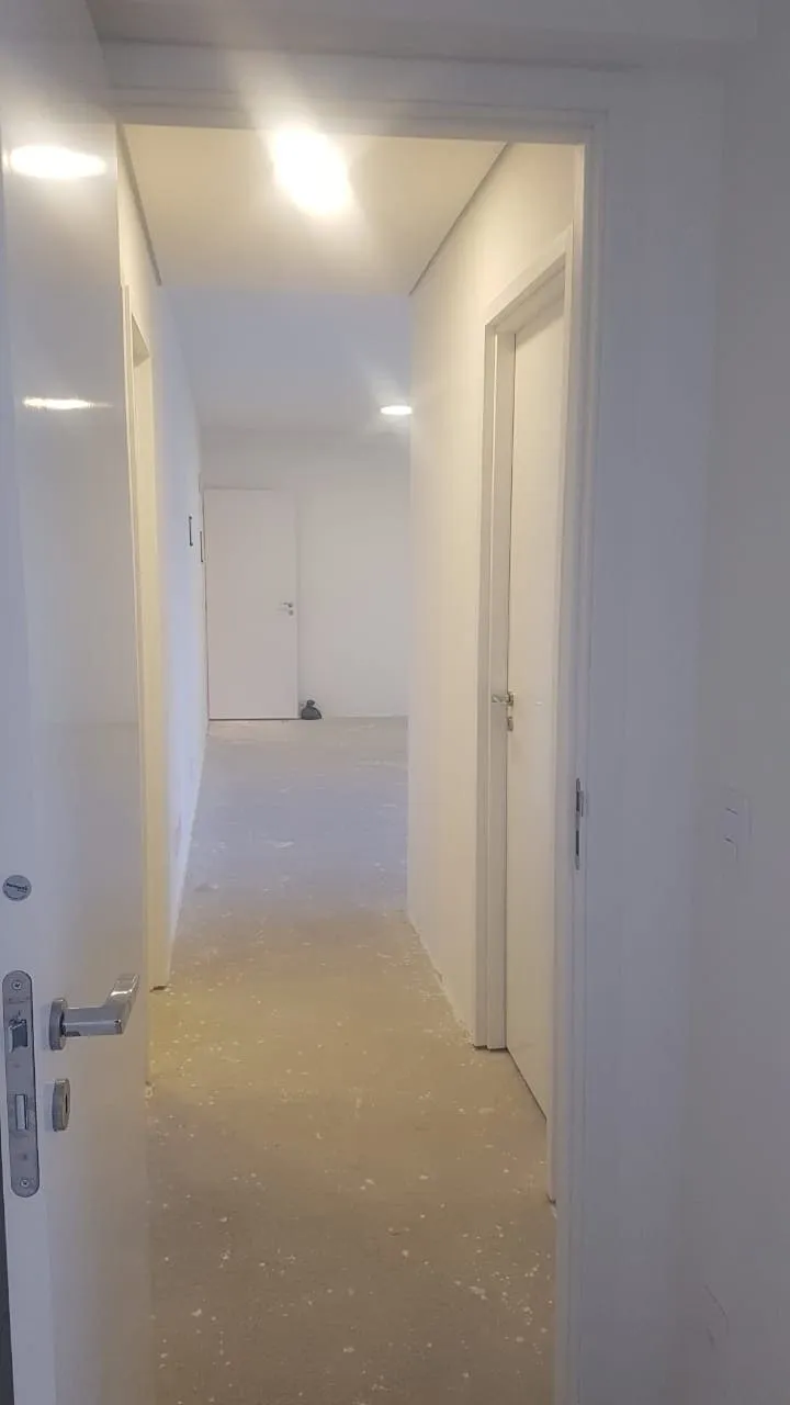 Corredor com portas brancas, luzes embutidas no teto e piso de contrapiso ainda cru, antes da reforma