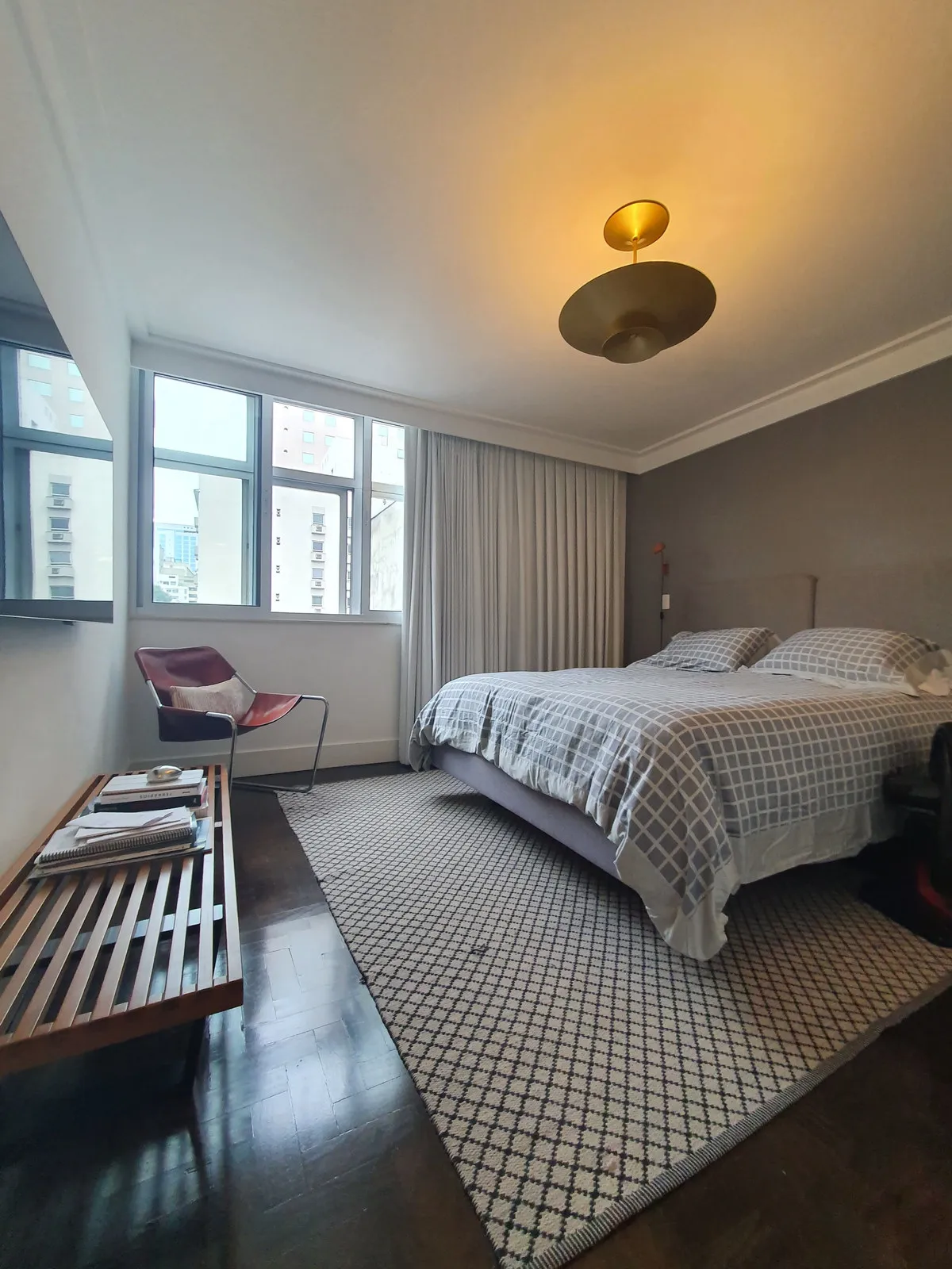 Quarto de casal com cama, parede cinza, janela ampla e piso de madeira escura, antes da reforma