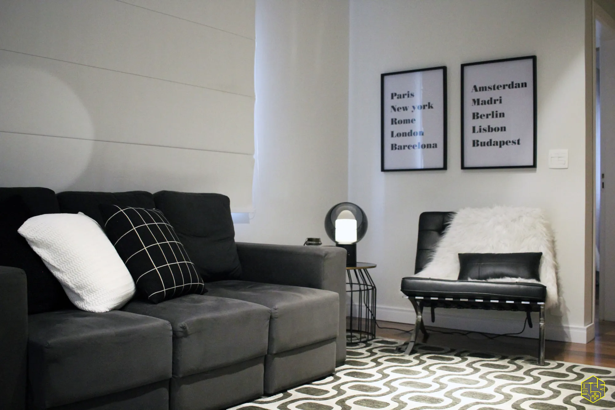 Sala de estar com sofá cinza, poltrona Barcelona preta e quadros de cidades