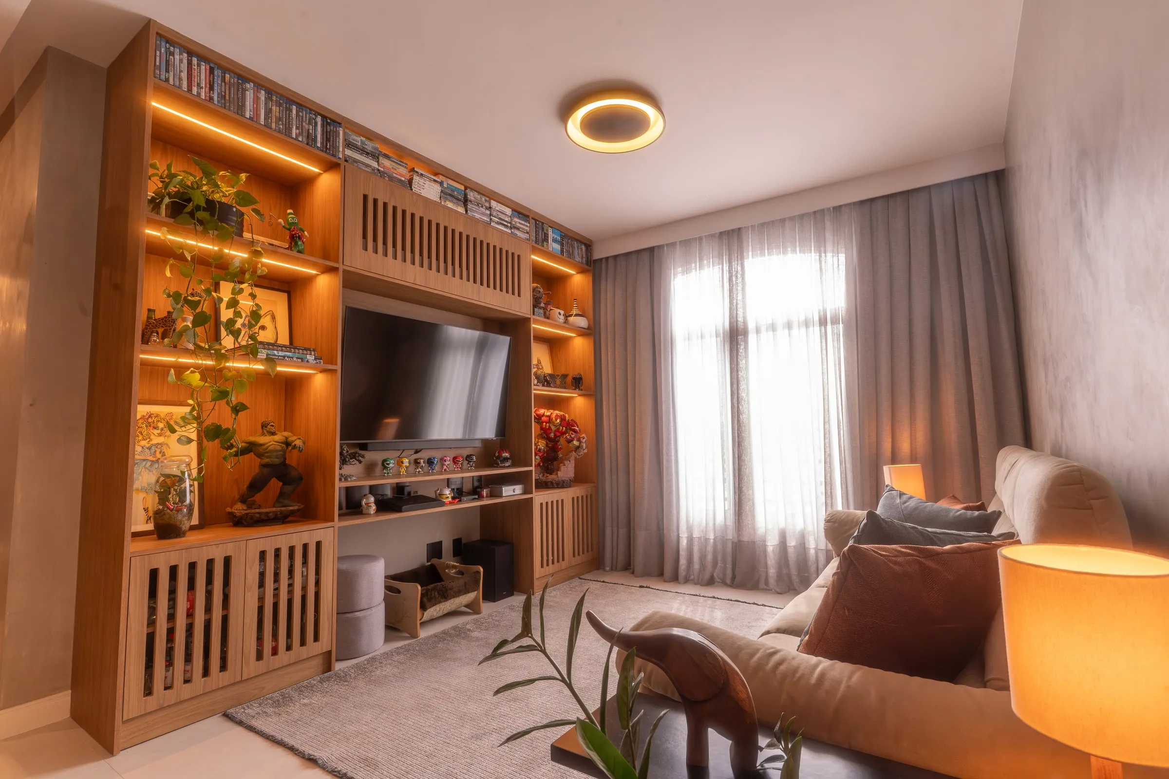 Sala de estar com estante de madeira iluminada, sofá e poltrona de couro caramelo
