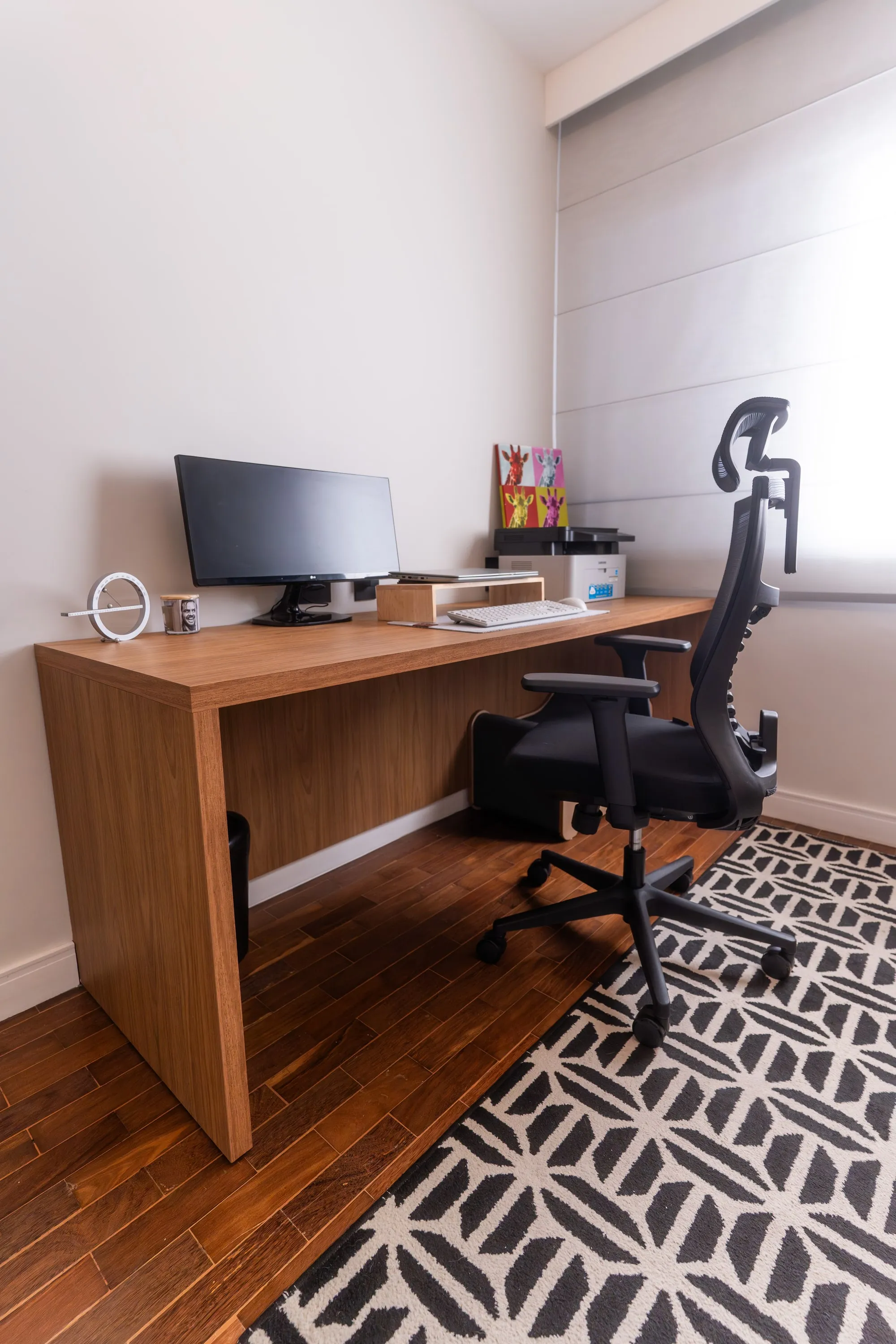 Home office com bancada de madeira suspensa, monitor ultrawide, cadeira ergonômica e tapete geométrico