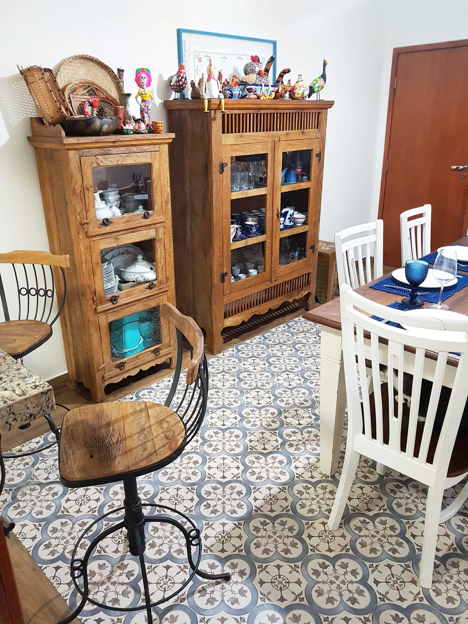Cristaleiras de madeira com louça e a coleção de aves no topo, ao lado da mesa de jantar, sobre piso de ladrilho hidráulico