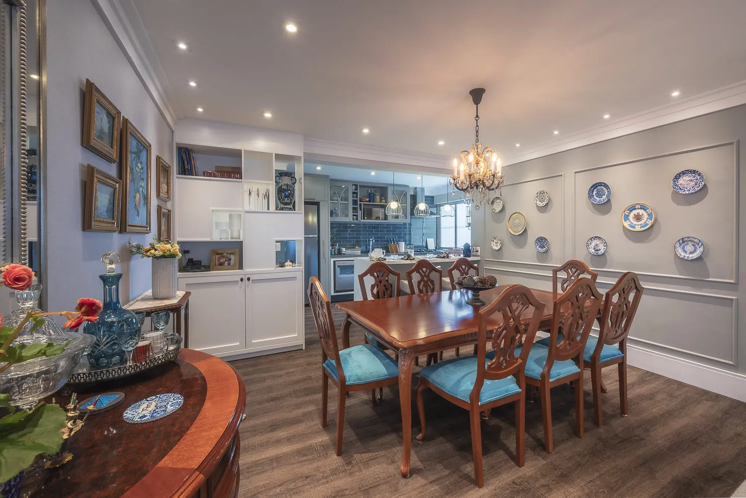 Sala de jantar clássica com mesa de madeira e cadeiras azul-turquesa, estante branca e lustre de cristal