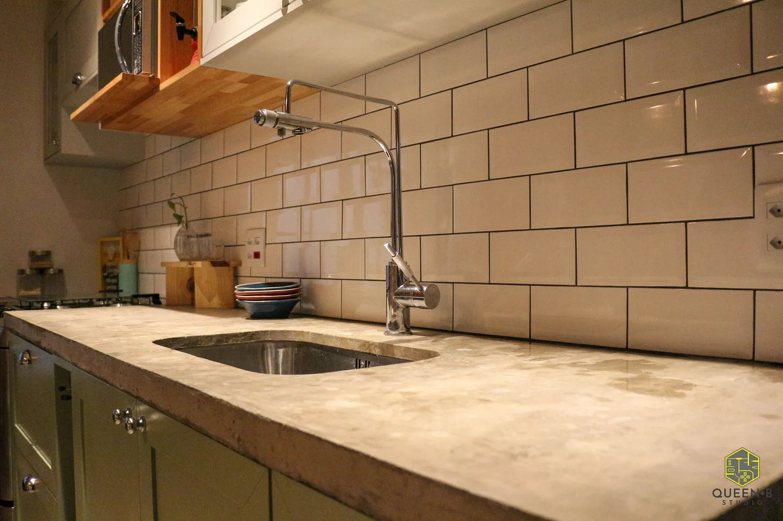 Detalhe de bancada de concreto com cuba de inox embutida, torneira cromada alta e azulejo de metrô branco ao fundo
