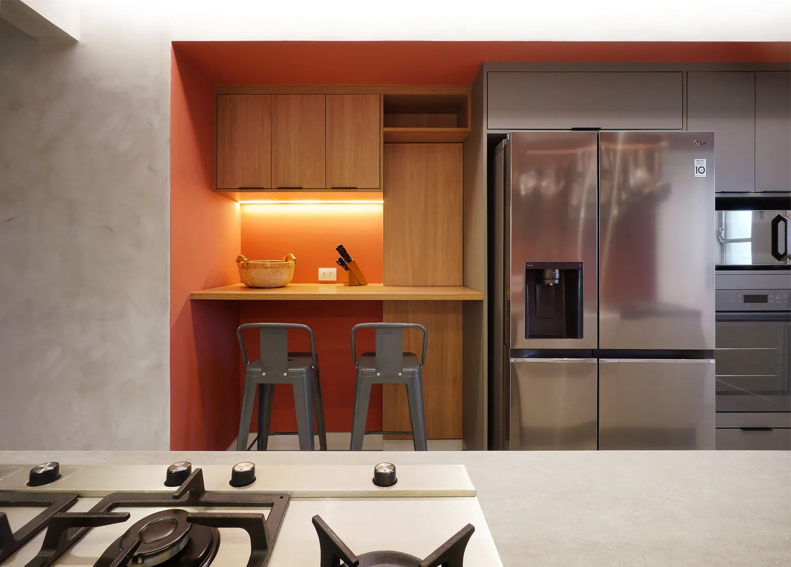 Cozinha com nicho de parede terracota, marcenaria amadeirada, bancada com banquetas de metal e geladeira inox