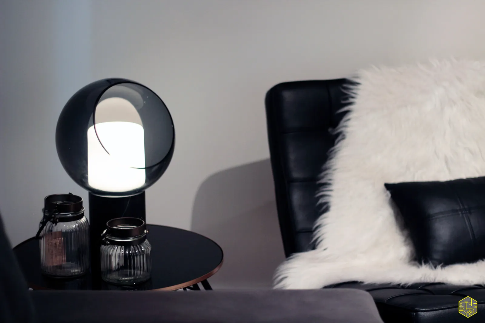 Detalhe de luminária de esfera de vidro preto acesa sobre mesa lateral, ao lado da poltrona de couro preta com pelo branco