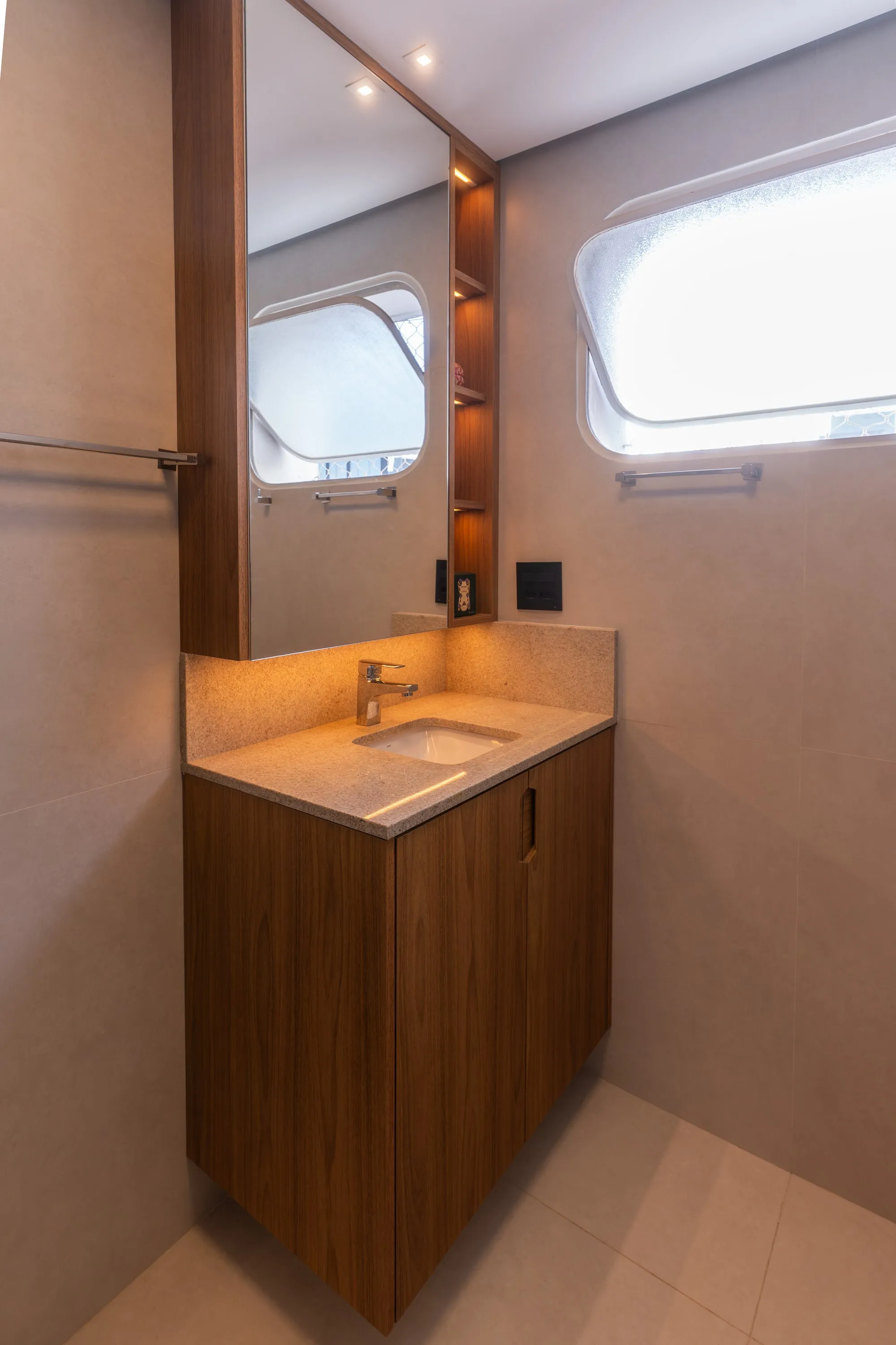 Lavabo com bancada de granito bege suspensa, marcenaria de madeira e espelho com nicho iluminado