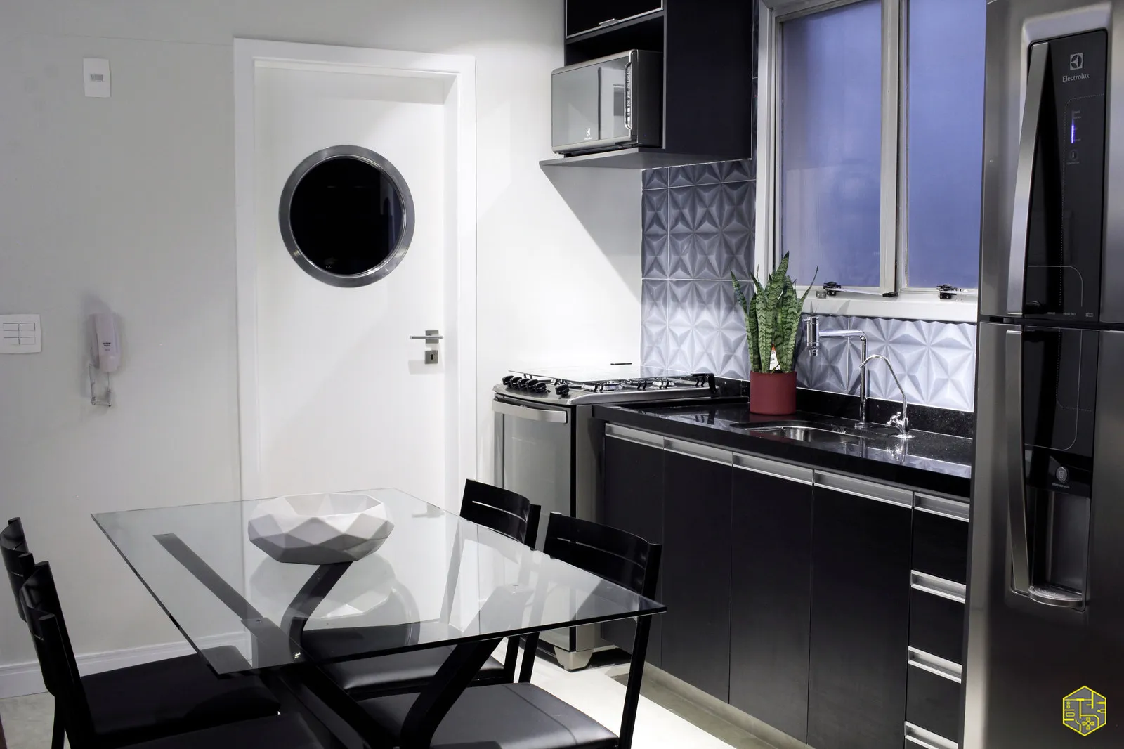 Cozinha com revestimento geométrico em relevo cinza, fogão inox, bancada de granito preto, cuba e planta em vaso vermelho