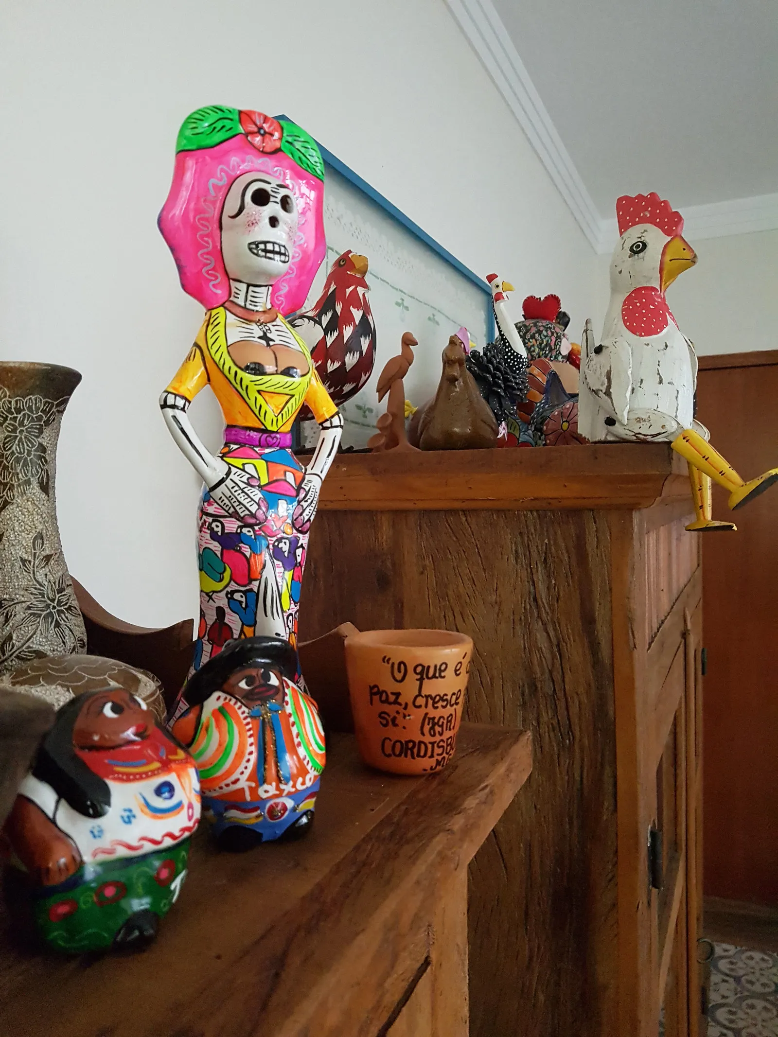 Detalhe do aparador de madeira com a coleção de galos de cerâmica e artesanato colorido da casa