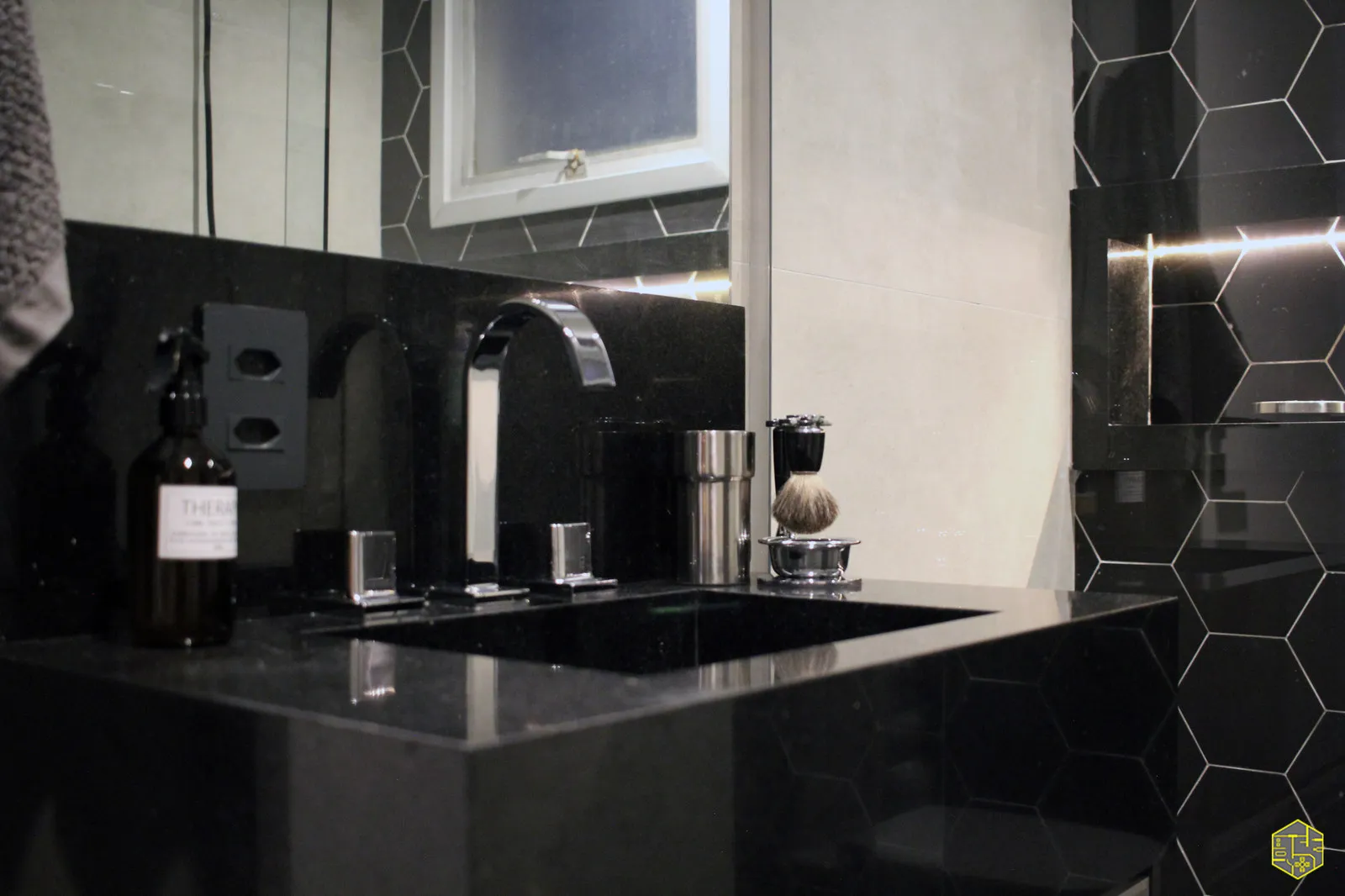 Bancada de banheiro em granito preto com cuba esculpida, torneira cromada, espelho e revestimento hexagonal preto