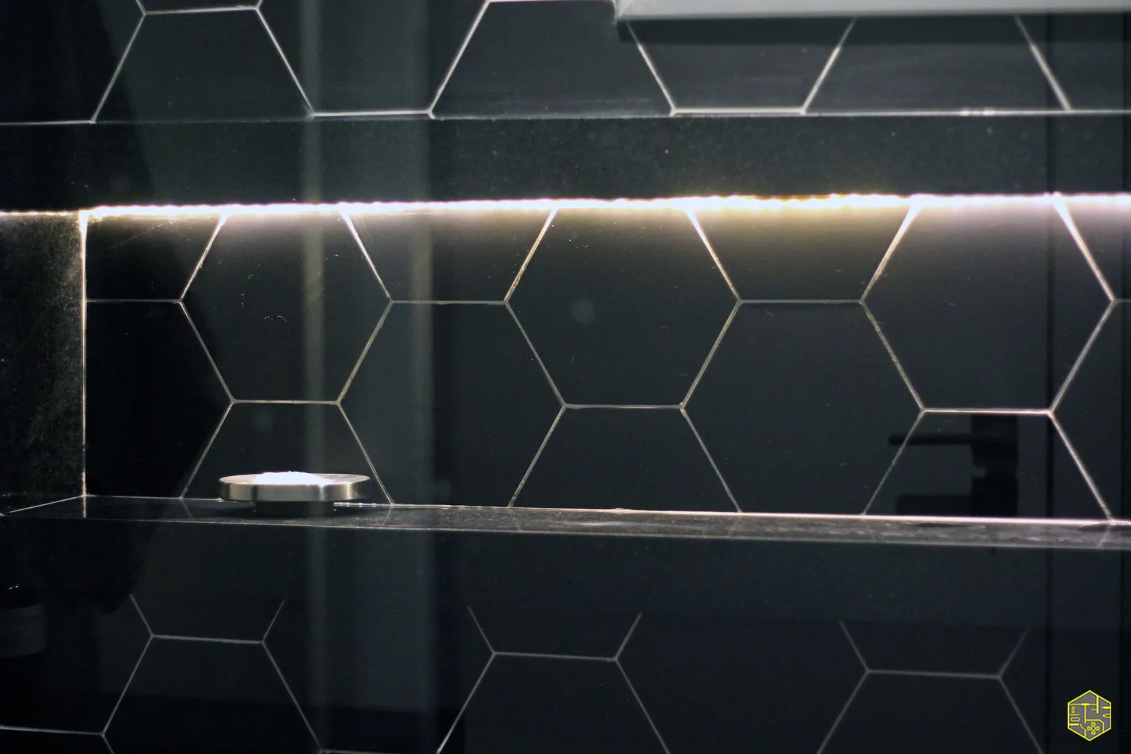 Detalhe do revestimento hexagonal preto do banheiro com fita de LED iluminando o nicho de granito preto
