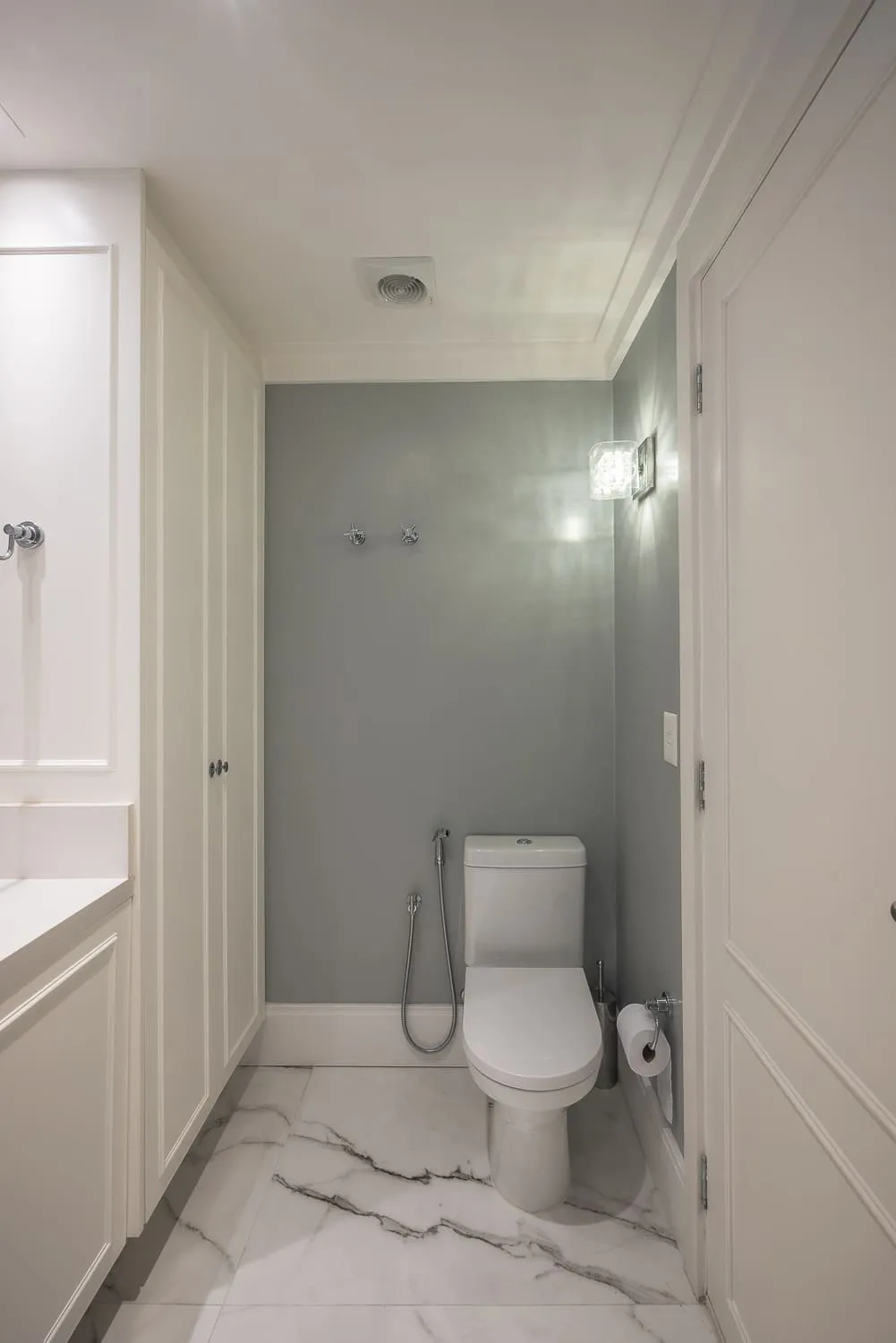 Lavabo com parede verde-acinzentada, vaso sanitário branco, marcenaria off-white e piso de mármore