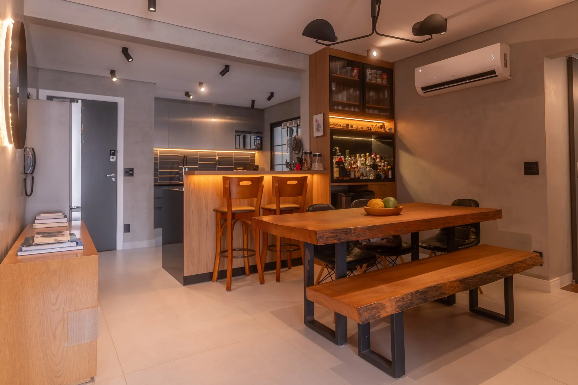 Sala de jantar integrada com mesa de madeira maciça, banco, cadeiras pretas, balcão com banquetas e cozinha ao fundo