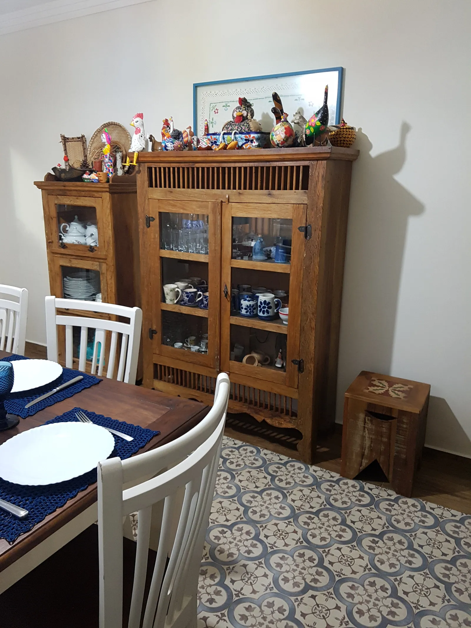 Cristaleiras de madeira rústica com louça azul e a coleção de aves no topo, ao lado da mesa de jantar